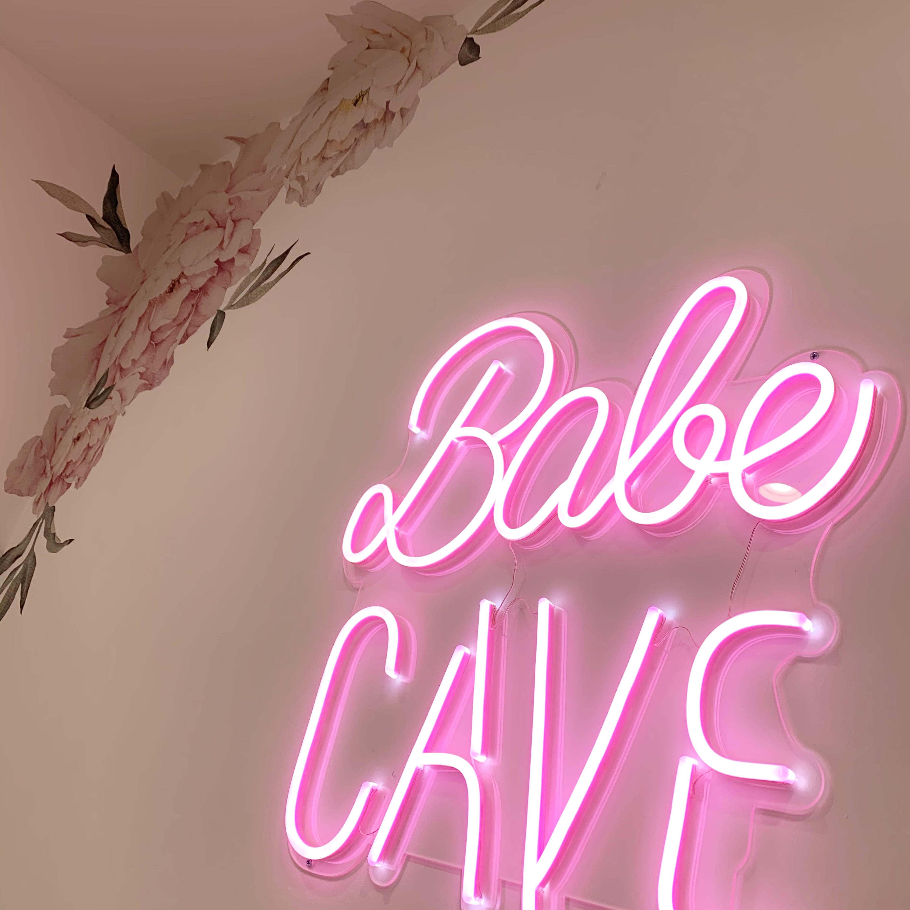 A pink neon sign reading "Babe Cave" is mounted on a wall adorned with floral decorations.