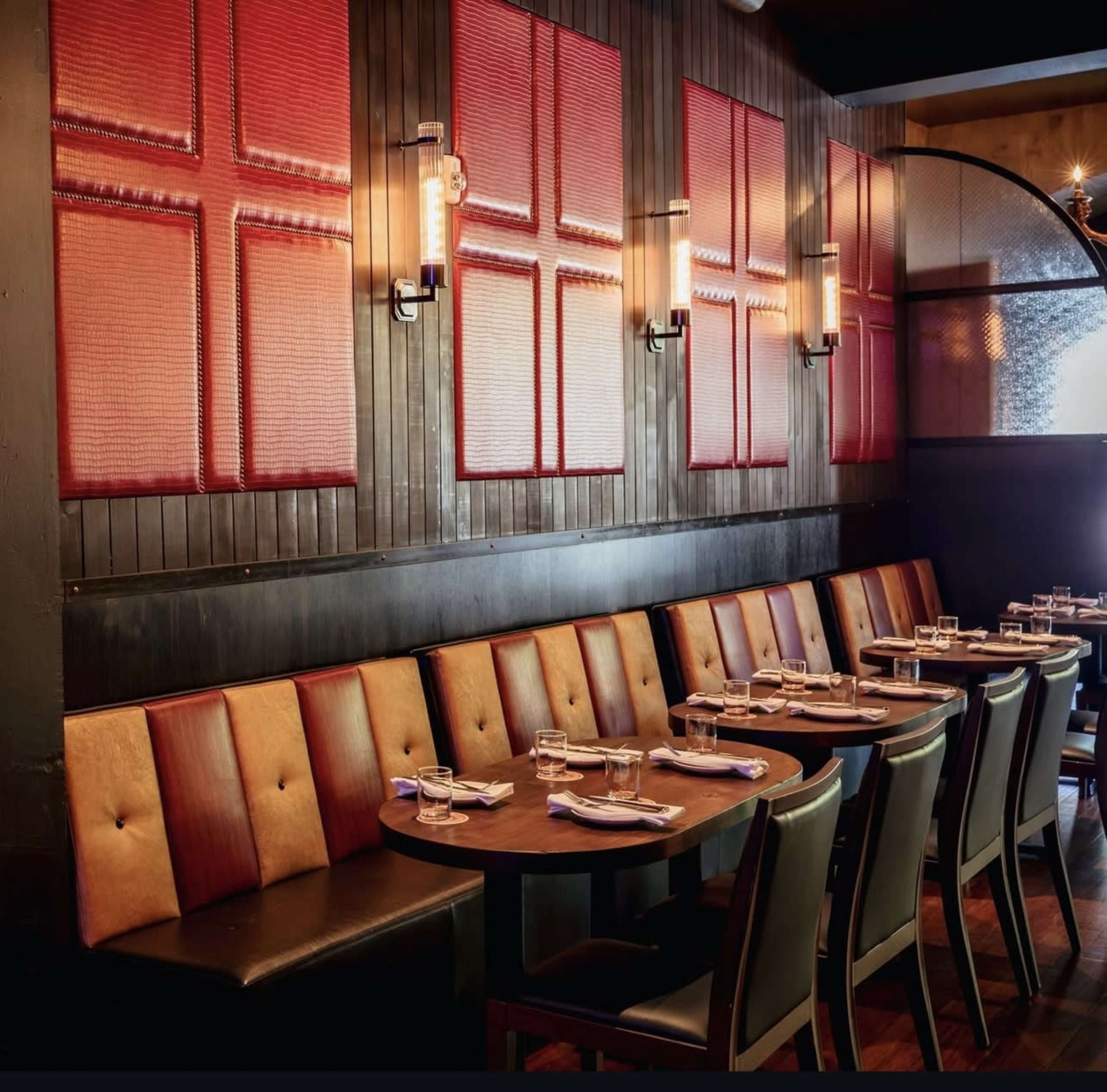The image shows a restaurant interior with a long cushioned bench along the wall and tables set with utensils and glasses.