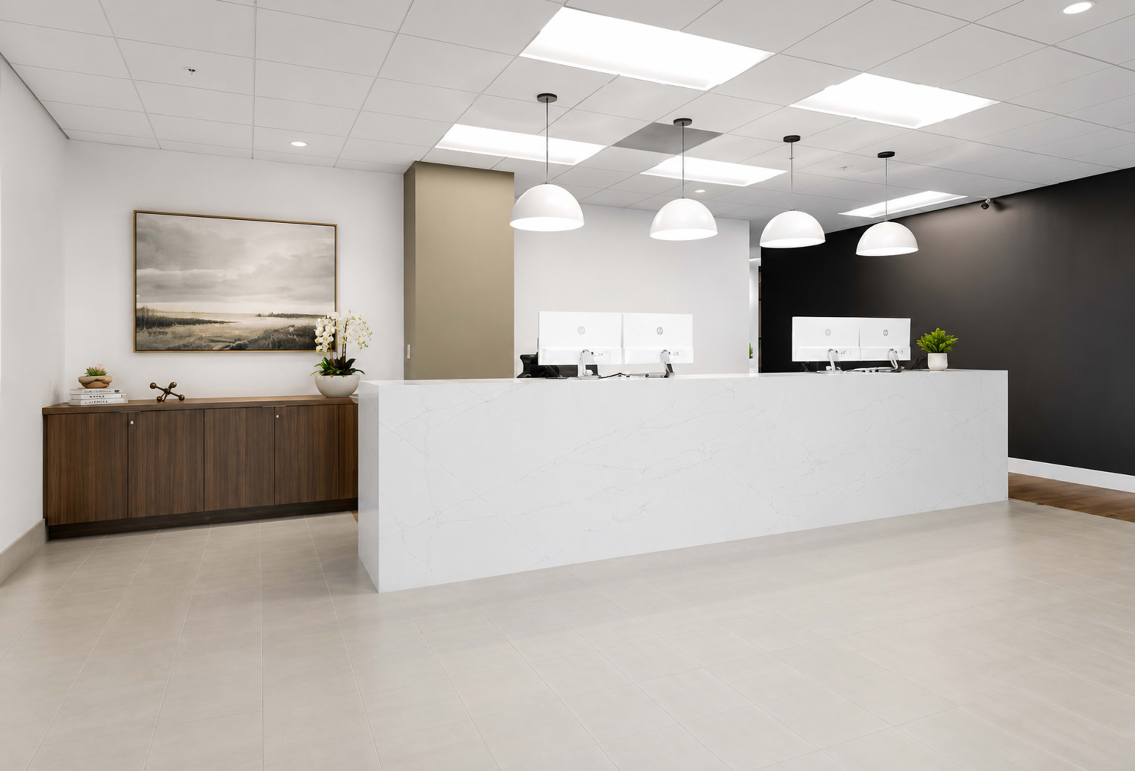 The image shows a modern reception area with a white marble front desk, several large pendant lights, and a dark accent wall.