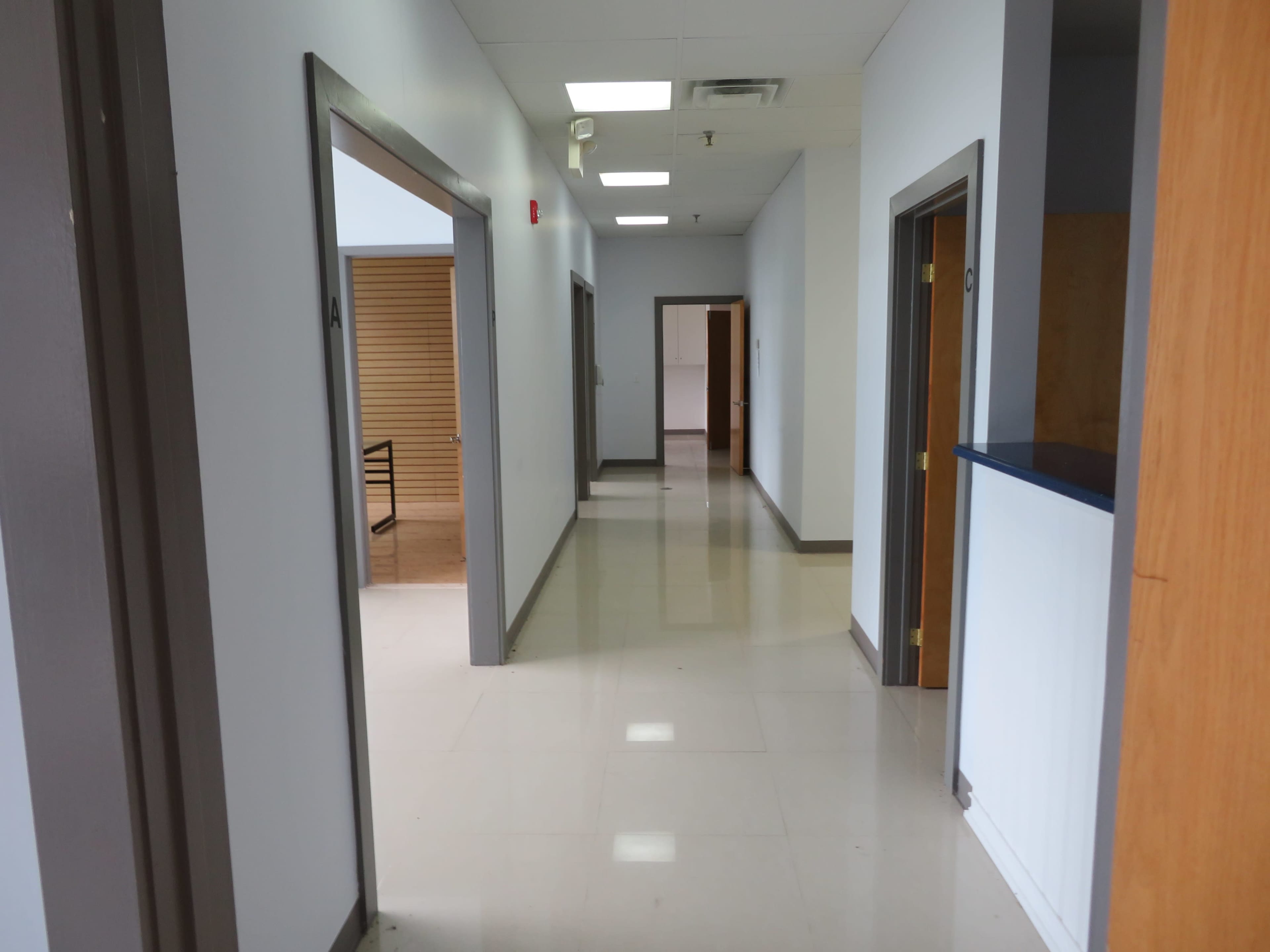 The image shows a long, empty hallway with doors on either side and a bright ceiling.