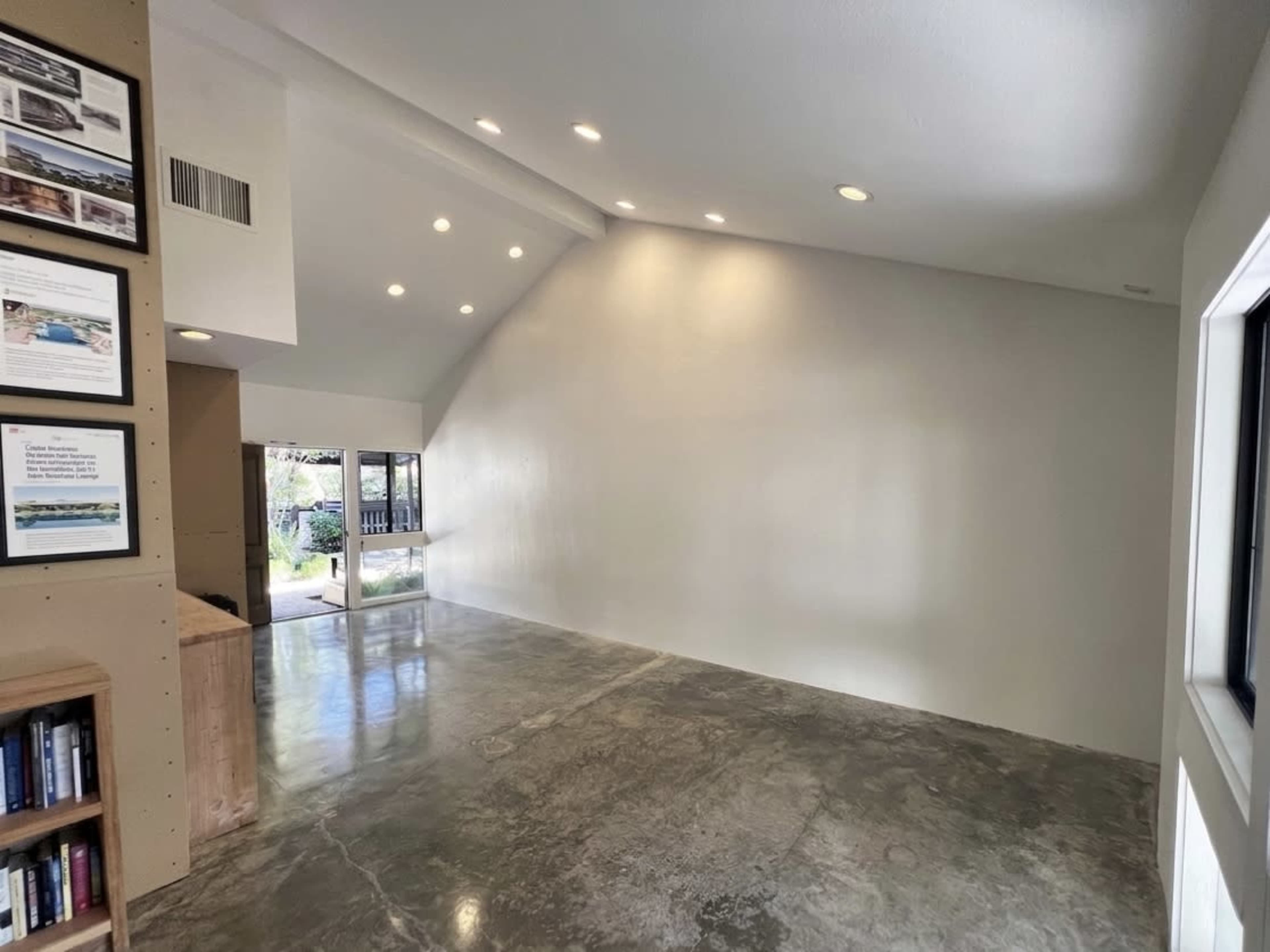 The image depicts a spacious, light-filled room with polished concrete flooring, high ceilings, and a large window on one side.