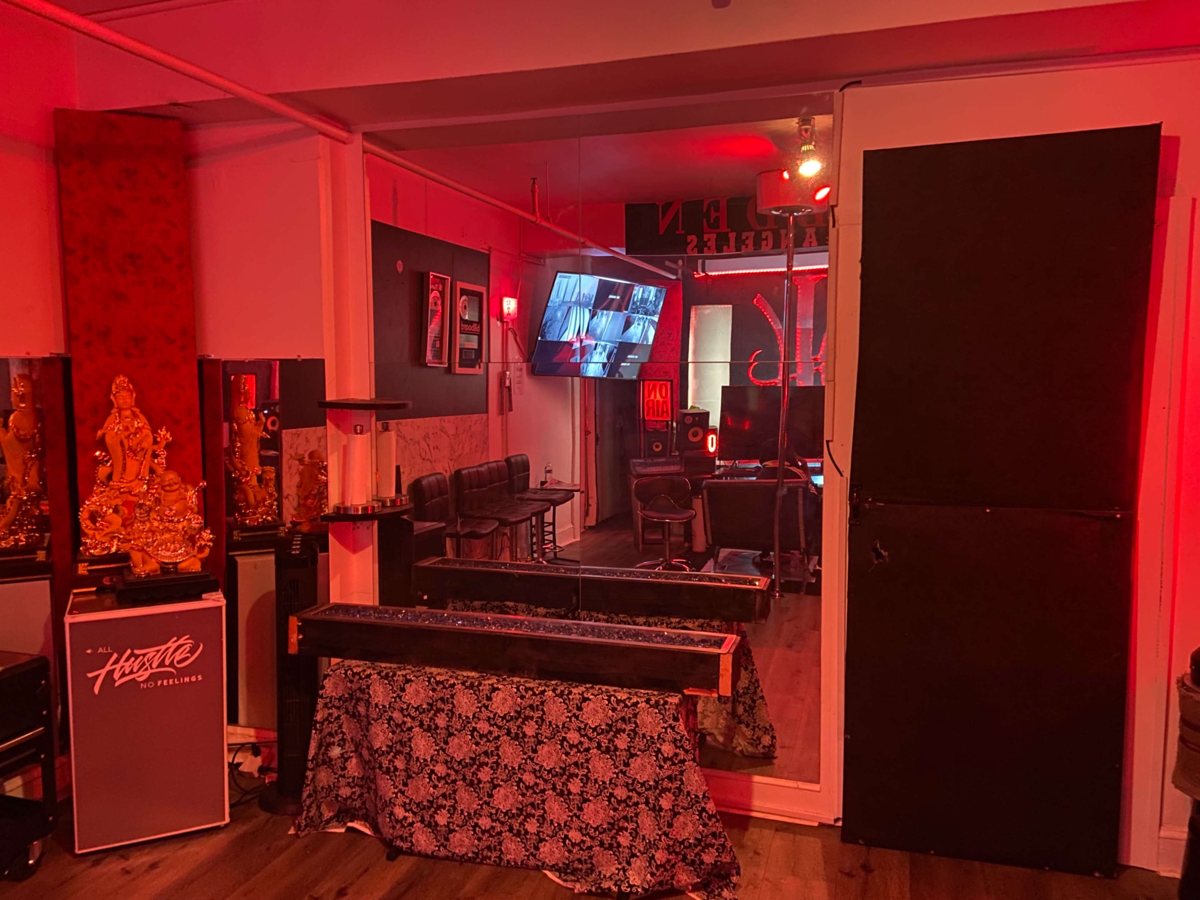 The image shows an interior of a dimly lit room with a large flat-screen TV on the wall, a black table covered with a patterned cloth, and seating arrangements in the background.