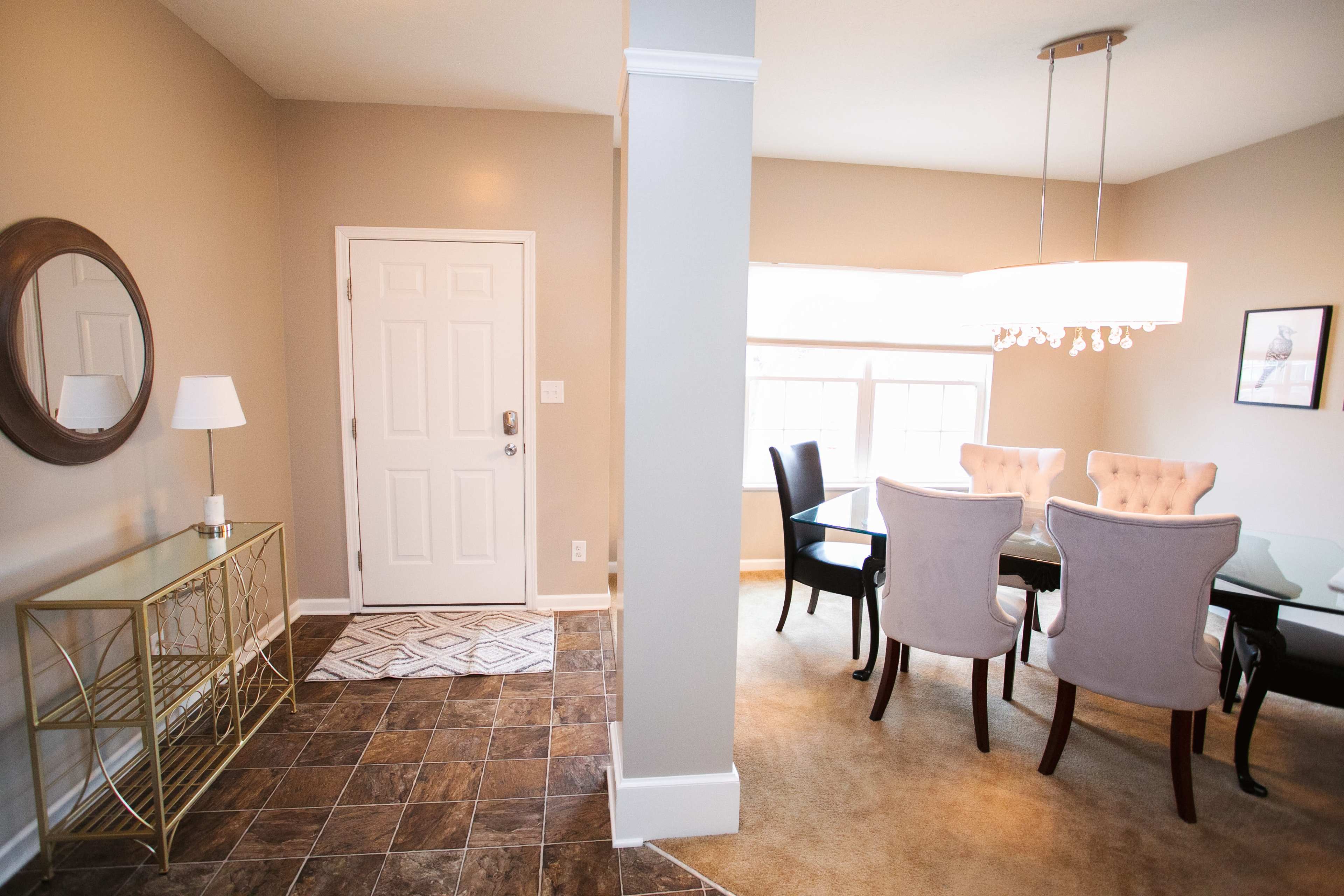 A foyer area leading to a dining space, featuring a table with chairs, a mirror on the wall, and a decorative light fixture.