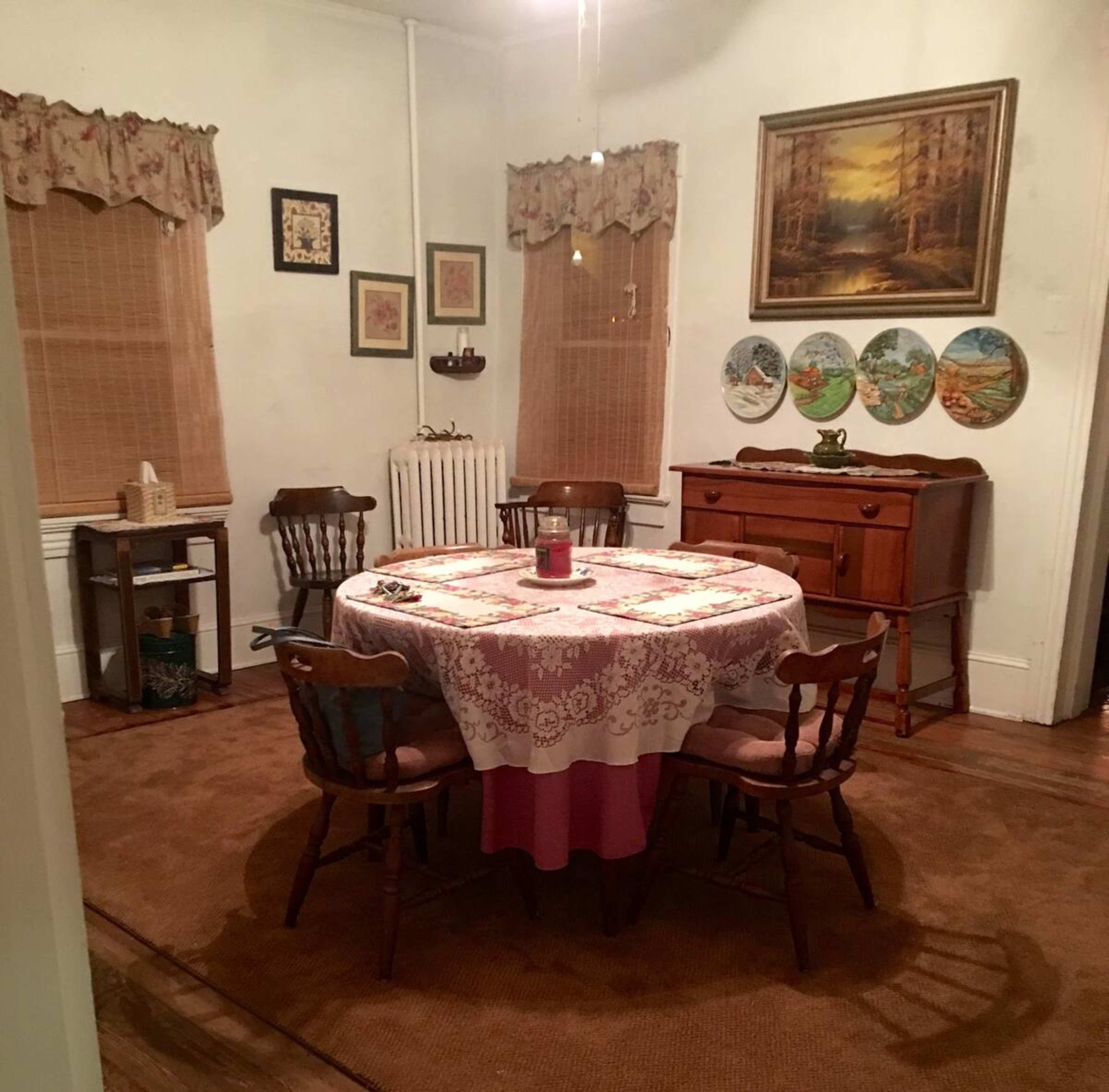 A cozy dining room with a round table set in the center, surrounded by wooden chairs, and adorned with framed artwork and decorative plates on the walls.