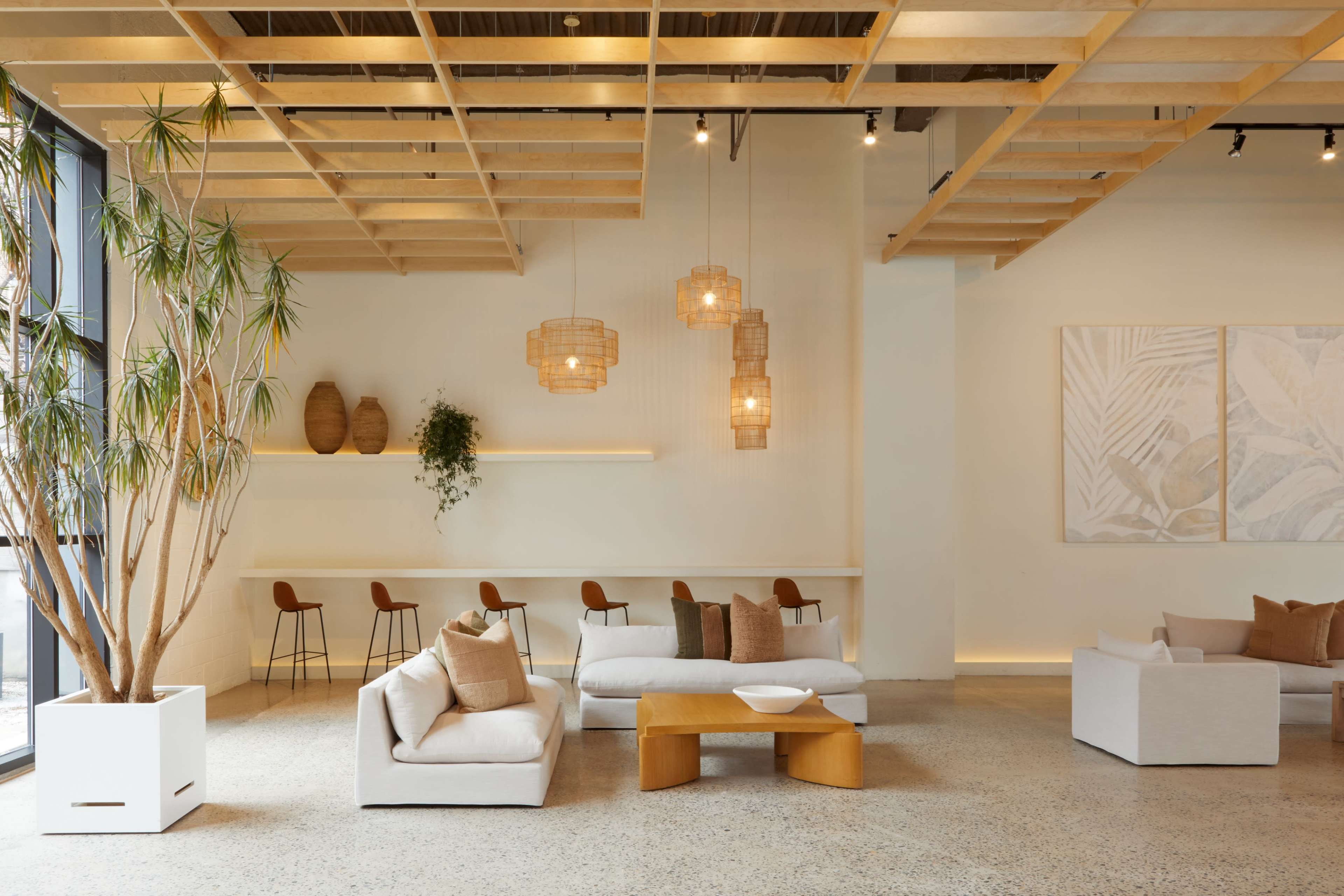 A modern lounge area features neutral-toned sofas with cushions, wooden pendant lights, and a decorative plant next to a minimalist table.
