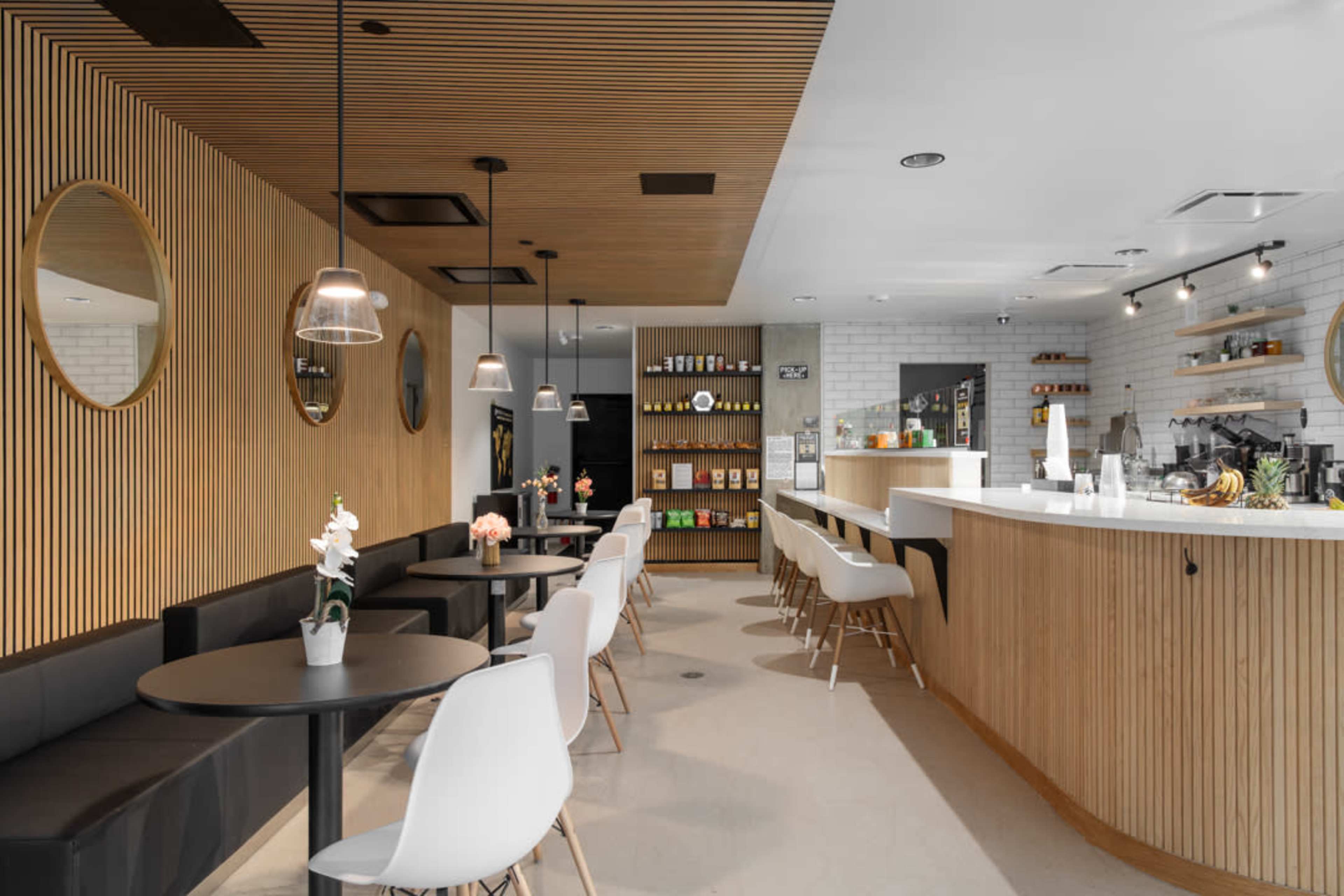 The image shows a modern café interior with wooden accents, circular mirrors, a sleek counter, and seating arrangements at tables and a bar.