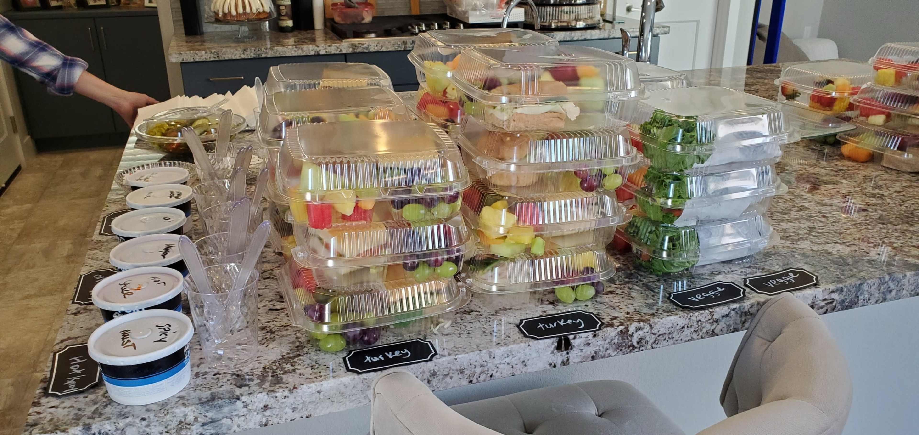 Several stacked containers filled with assorted fruit and salad items displayed on a kitchen counter alongside labeled containers of dressing.