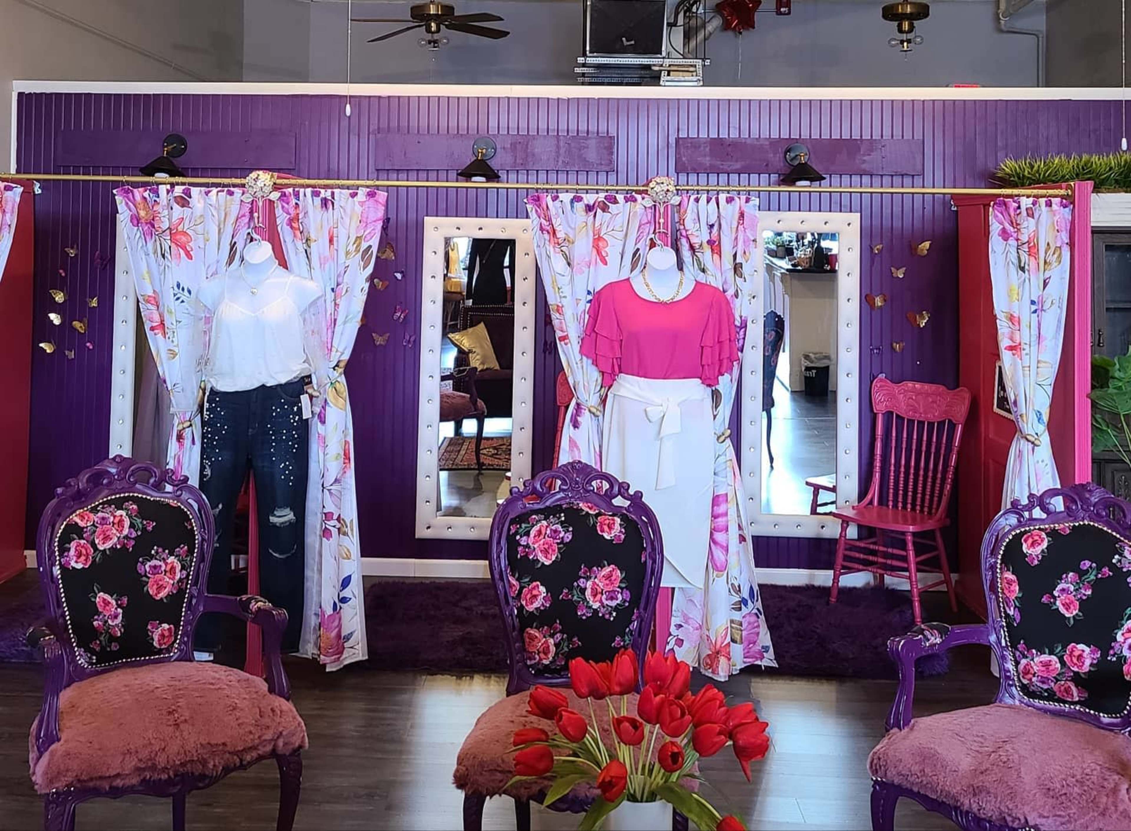 A boutique display featuring two mannequins dressed in colorful outfits, surrounded by floral curtains and mirrors in a vibrant interior setting.