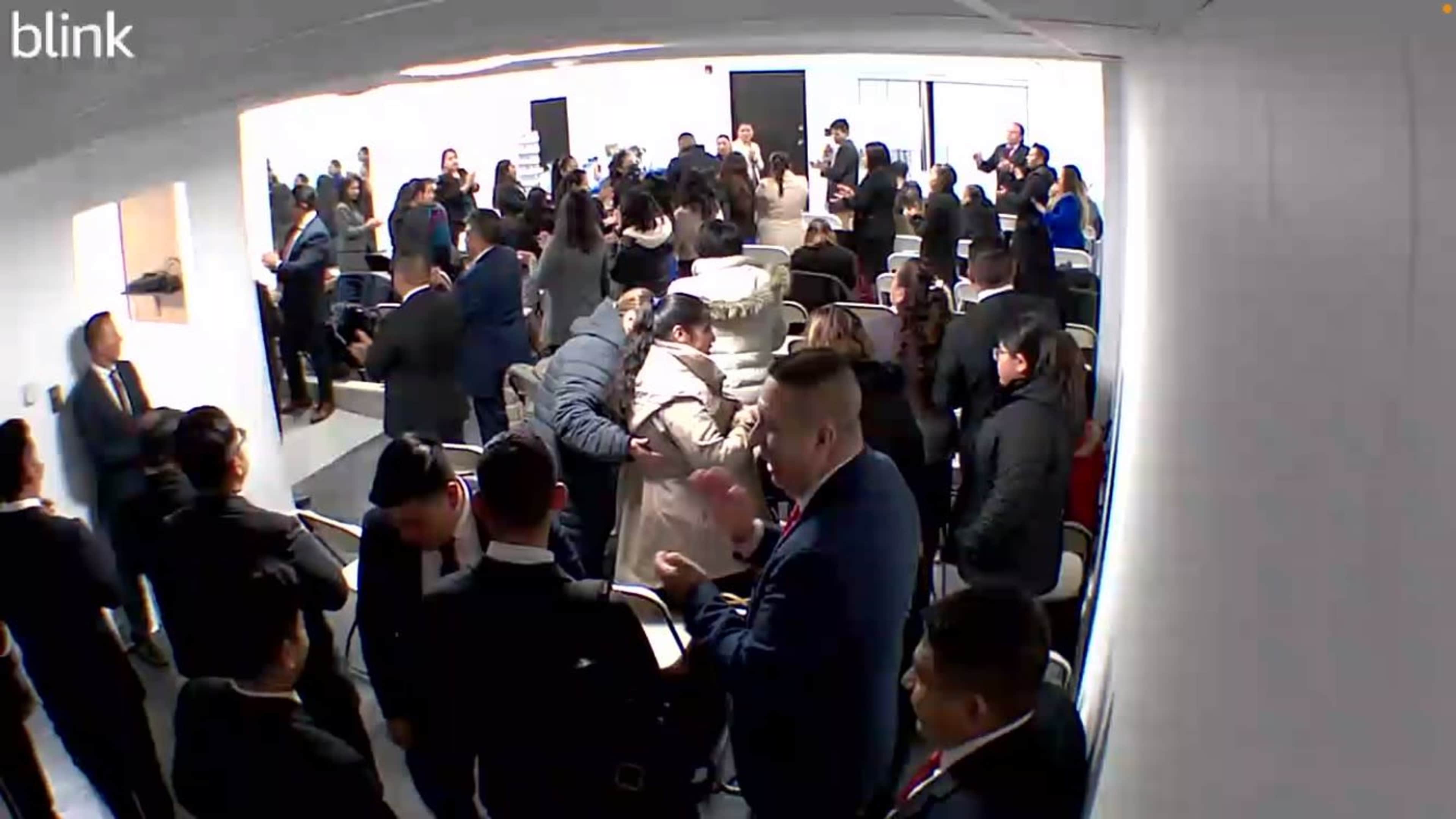 A large group of people is gathered in a room, interacting and mingling among chairs and standing areas.