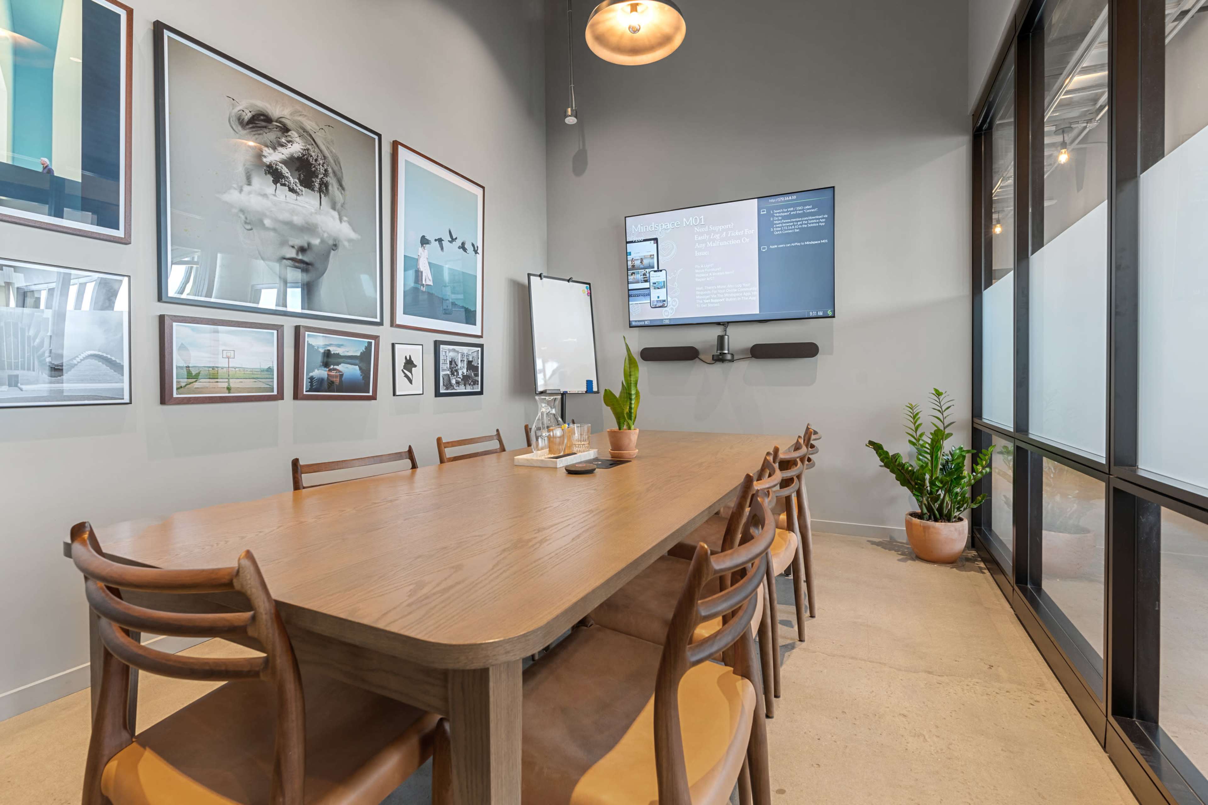 A conference room features a large wooden table surrounded by chairs, with framed photographs on the walls and a TV mounted on one side.