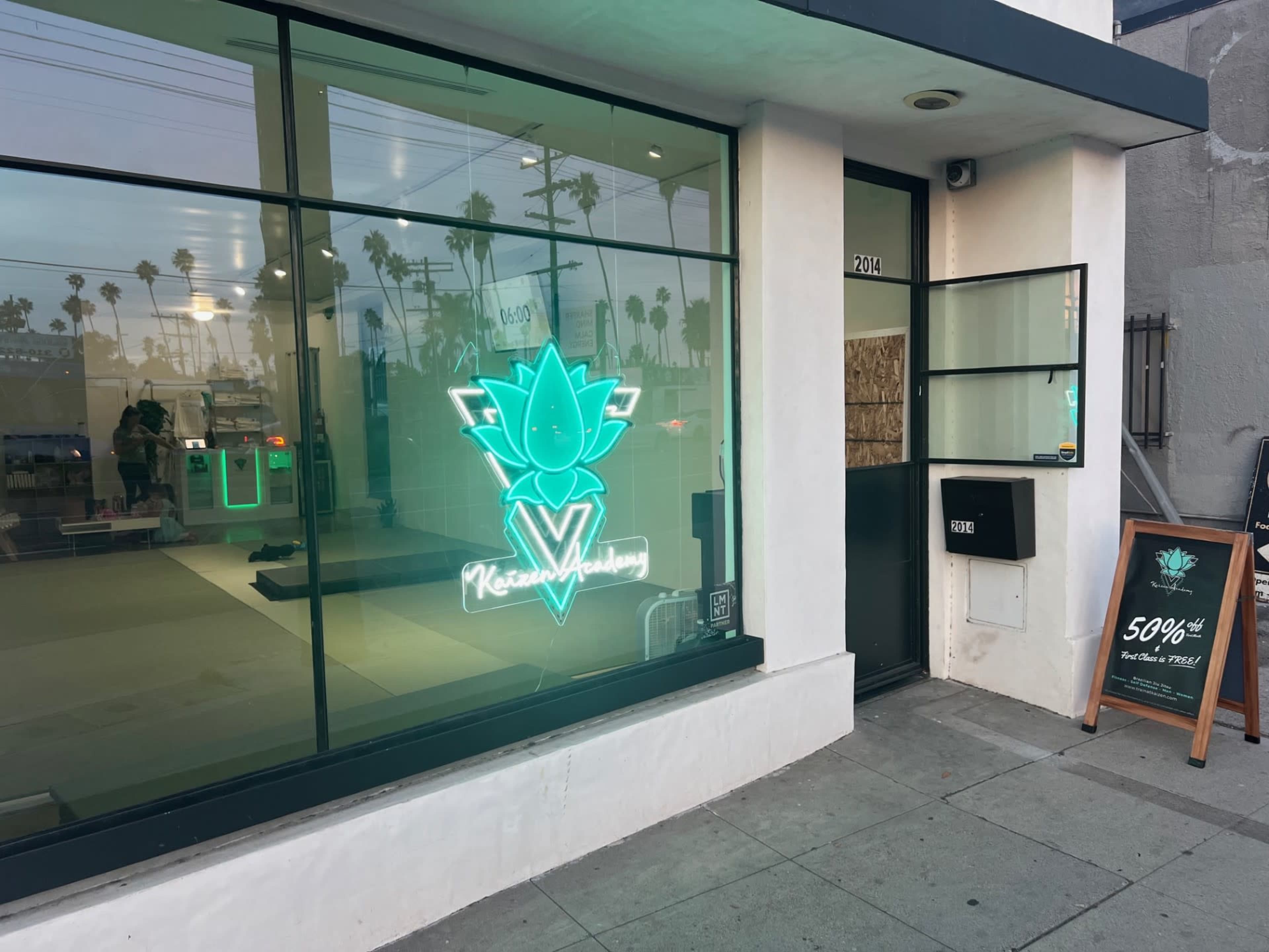 The image shows a storefront with a large glass window featuring a neon green logo of a lotus flower and the name "Kreator Academy."