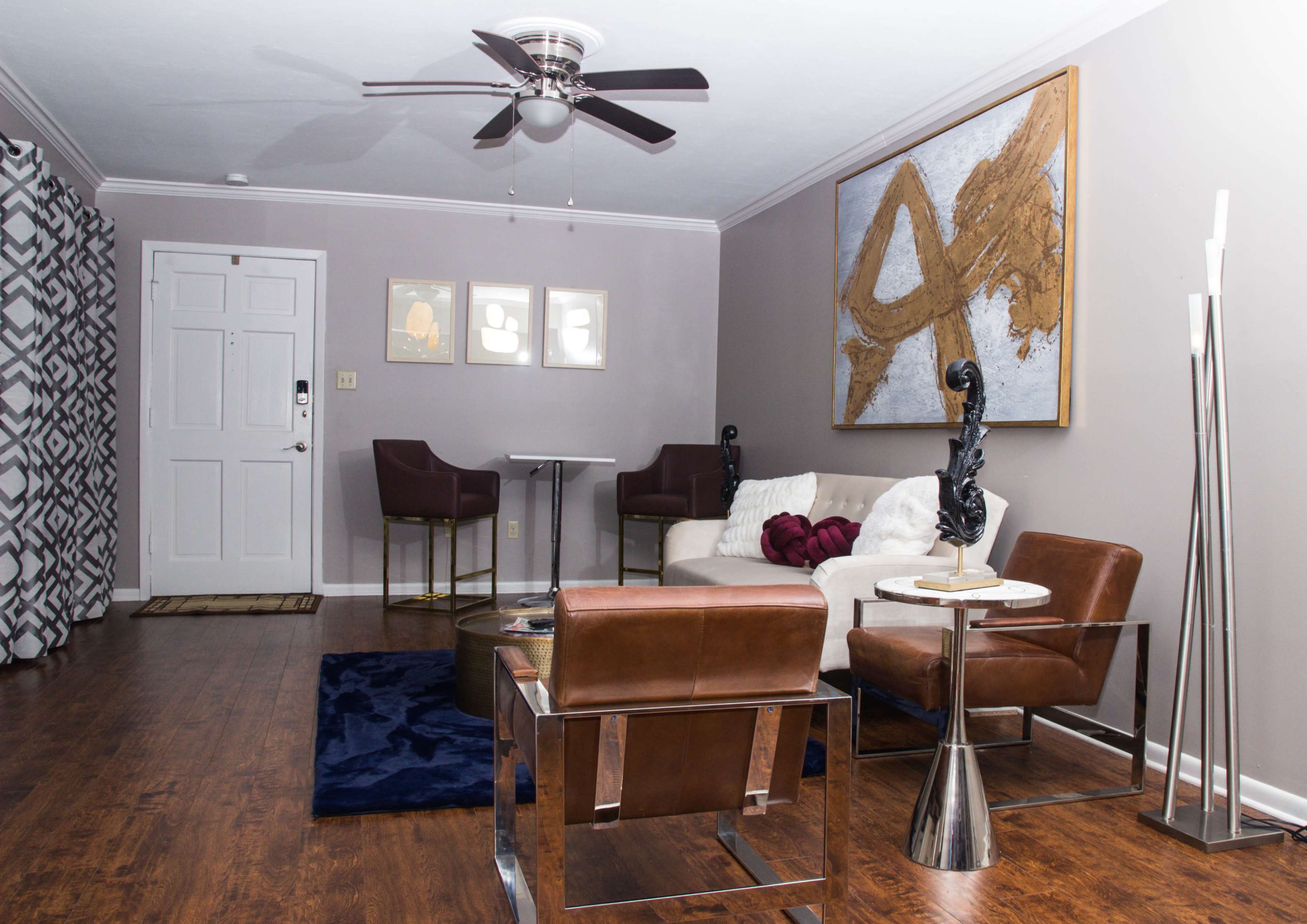 A modern living room featuring a brown leather armchair, a sleek glass-top table, and a decorative wall with abstract art.