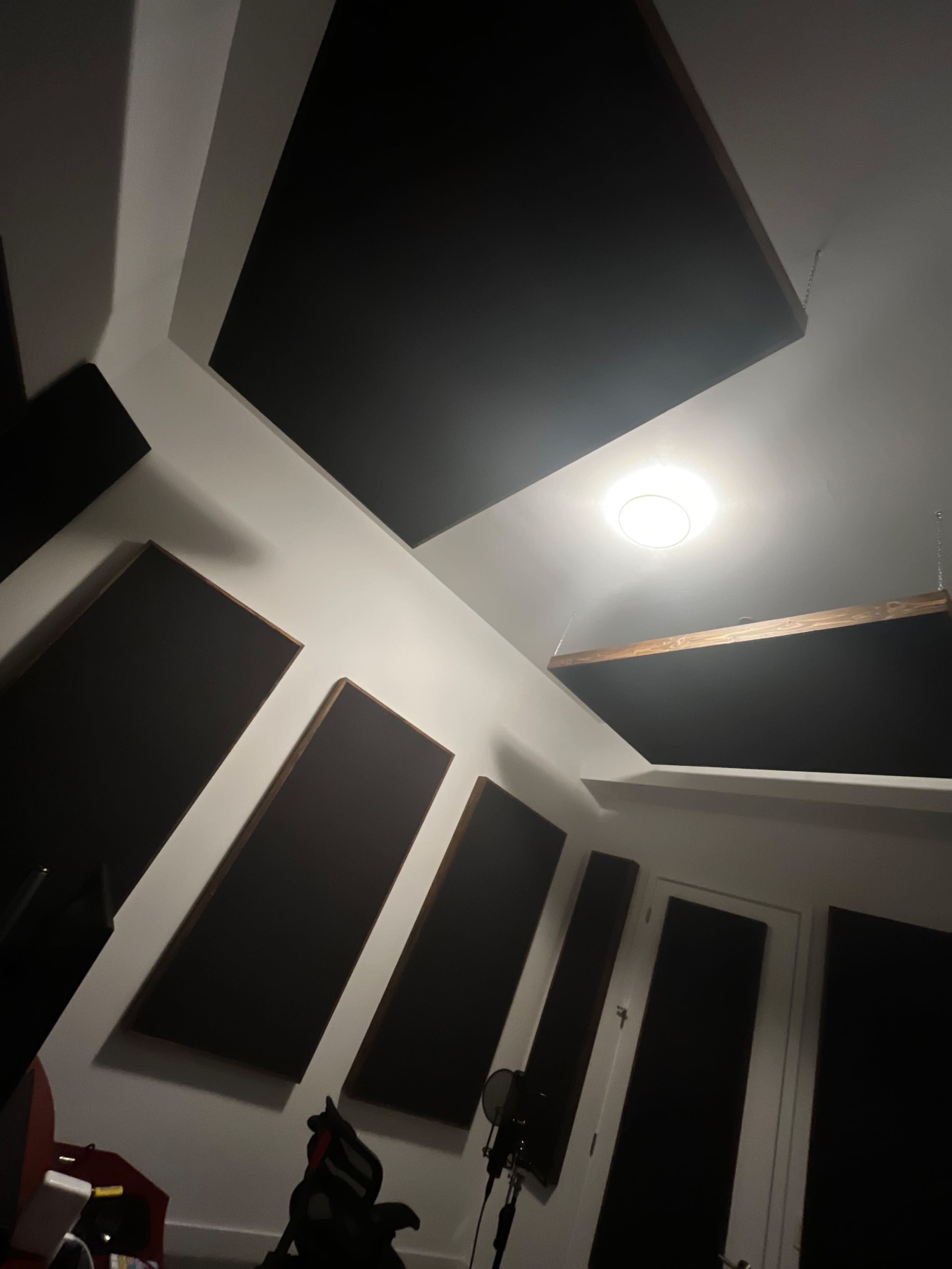 The image shows a recording studio with soundproofing panels mounted on the walls and ceiling, and a microphone on a stand in one corner.