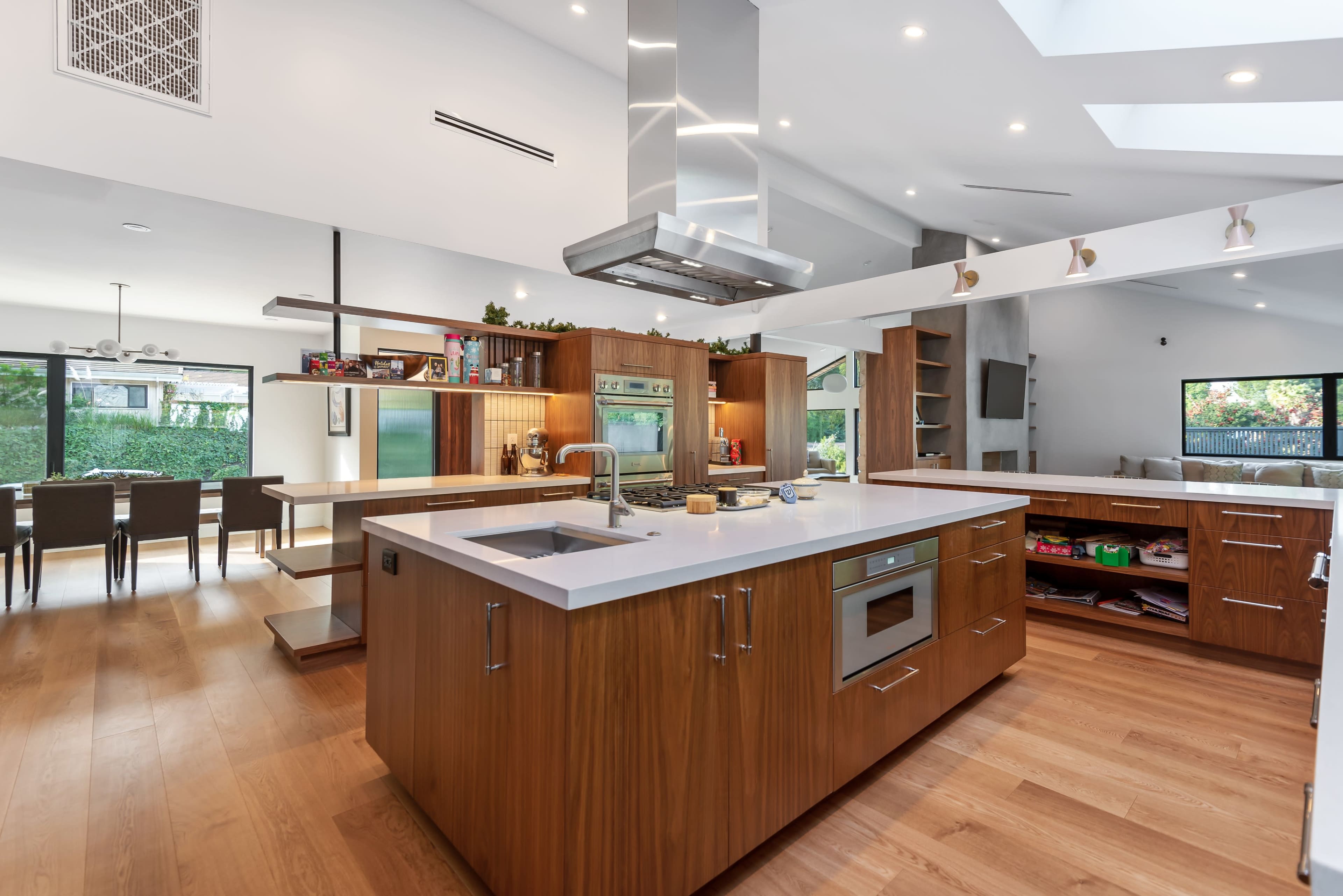 A modern kitchen featuring a large central island with a built-in oven, wooden cabinetry, and a dining area in the background.