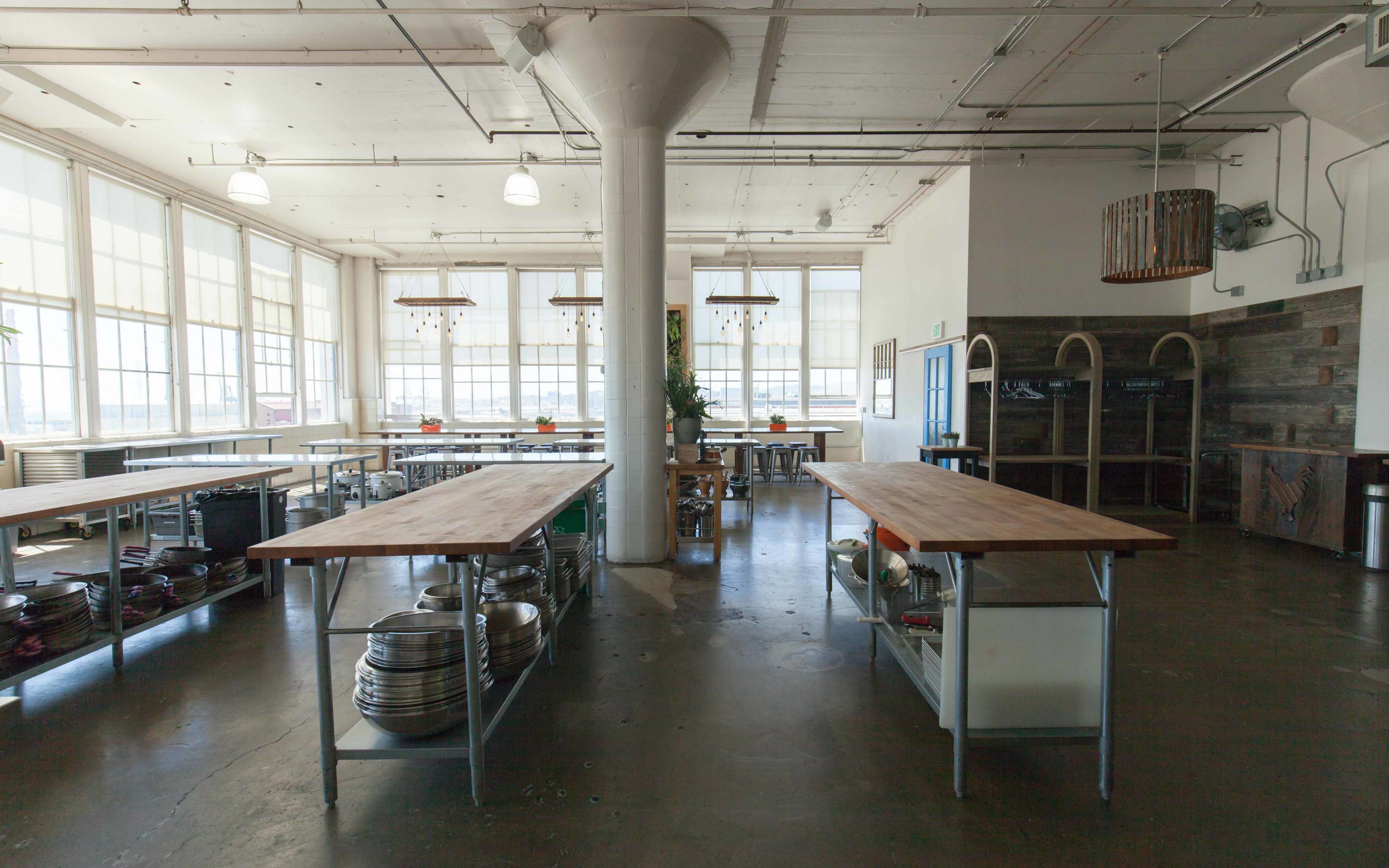 A spacious kitchen with stainless steel tables, large windows, and various kitchen utensils arranged on shelves.