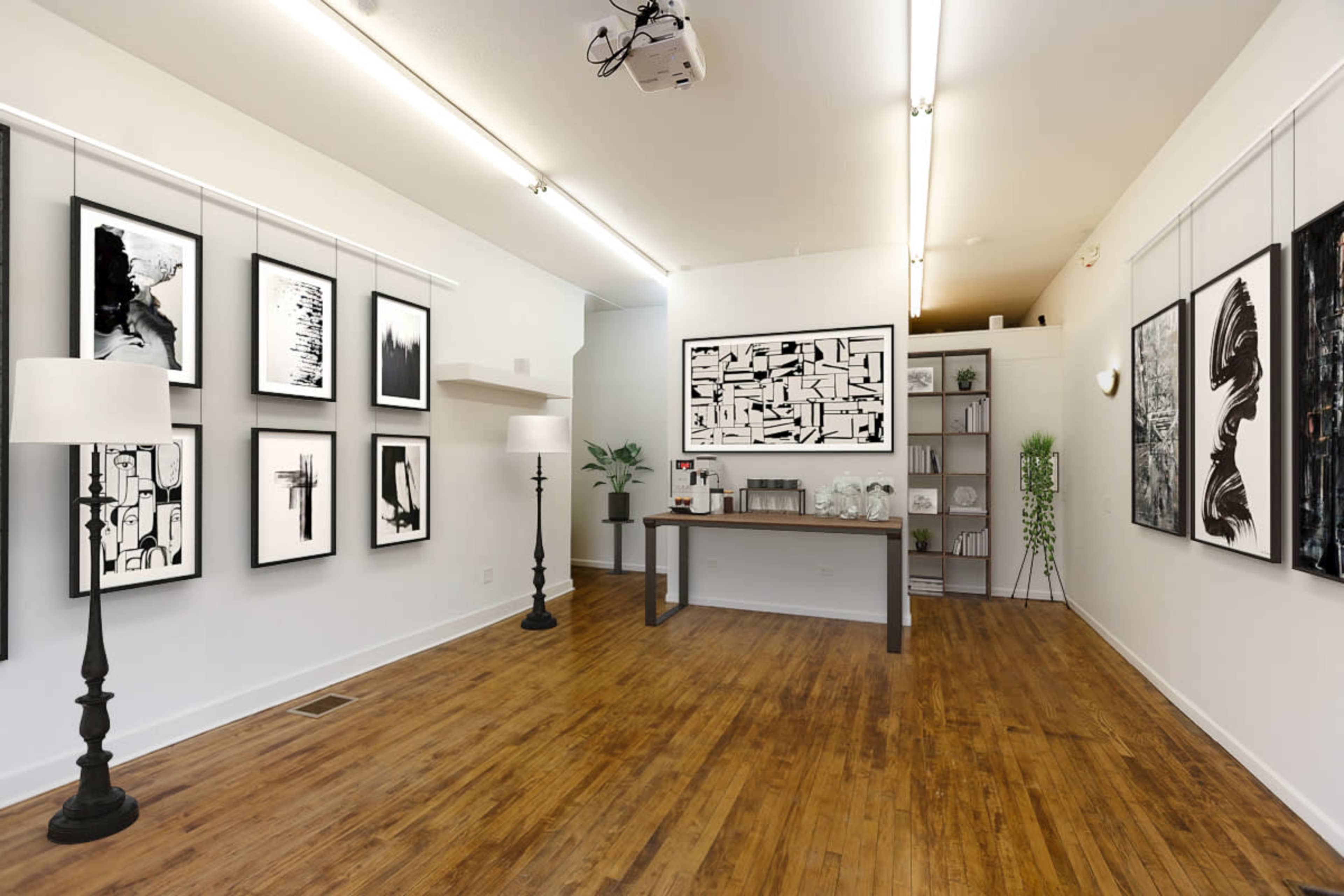 A modern gallery space with black and white artwork displayed on the walls, wooden flooring, and a central table with decorative items.