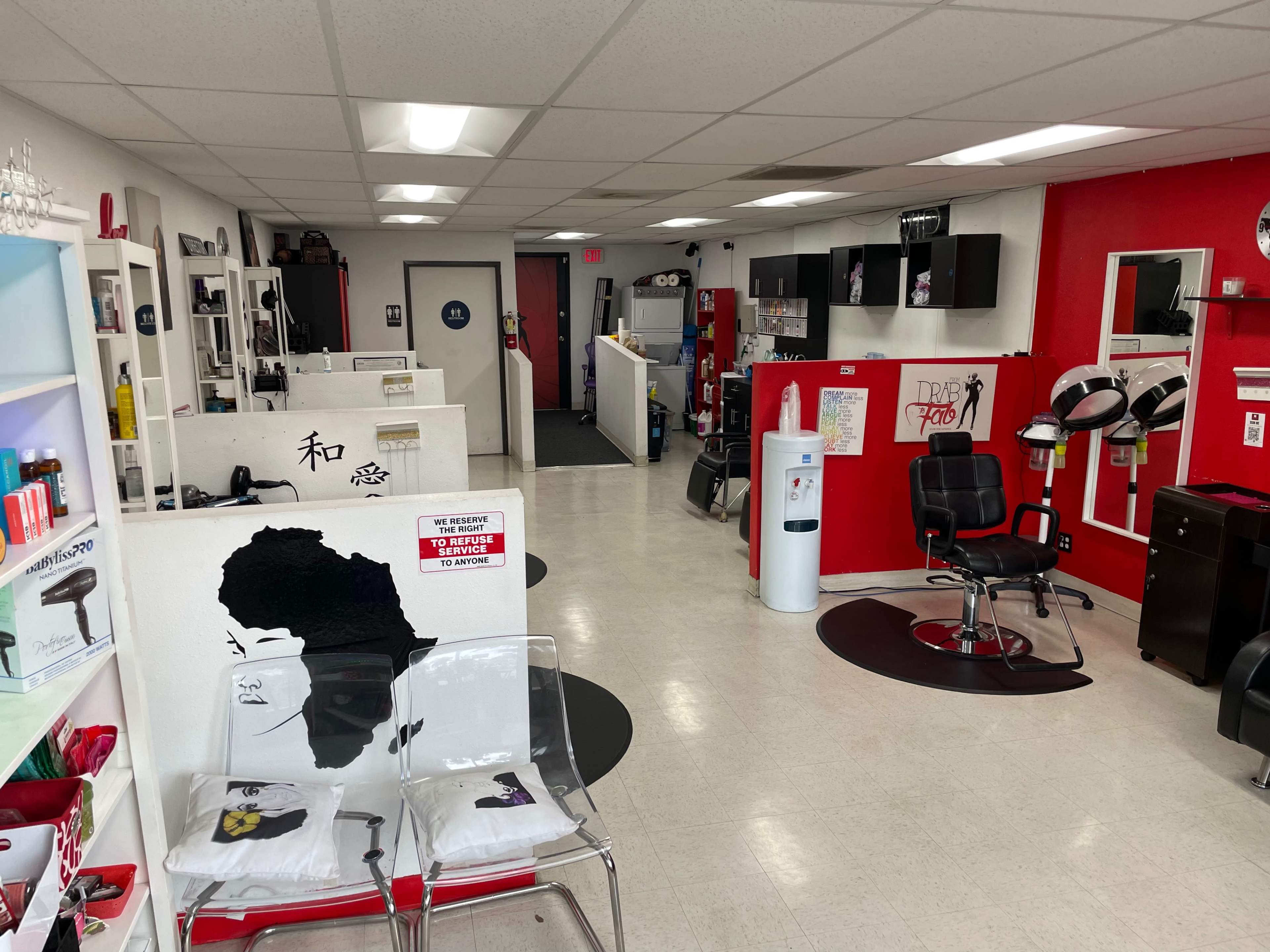 An interior view of a hair salon with styling chairs, workstation setups, and a reception area, featuring a mix of white and red walls.