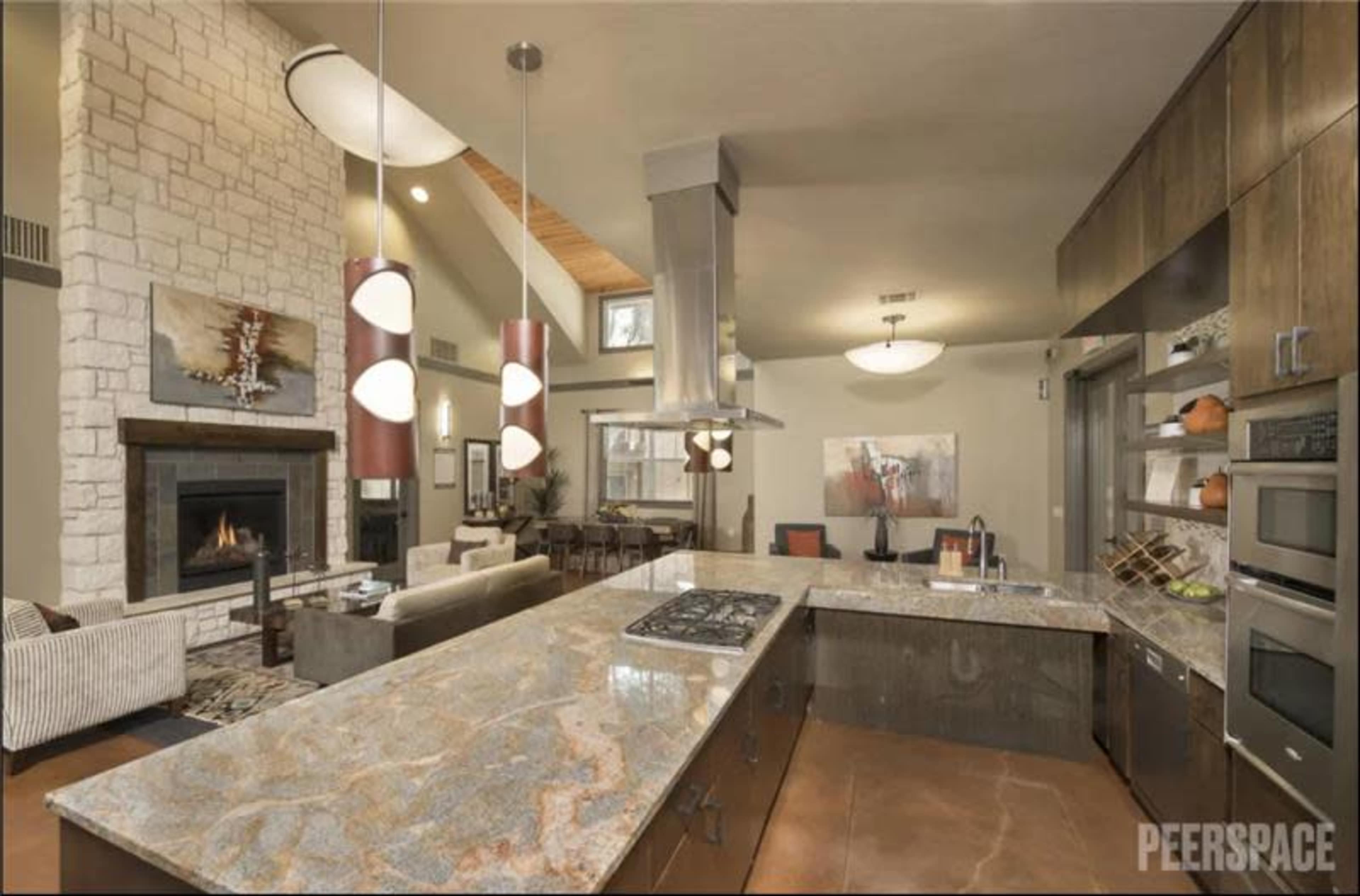 The spacious kitchen features a large granite island with a stovetop, modern fixtures, and a view of a cozy living area with a fireplace.