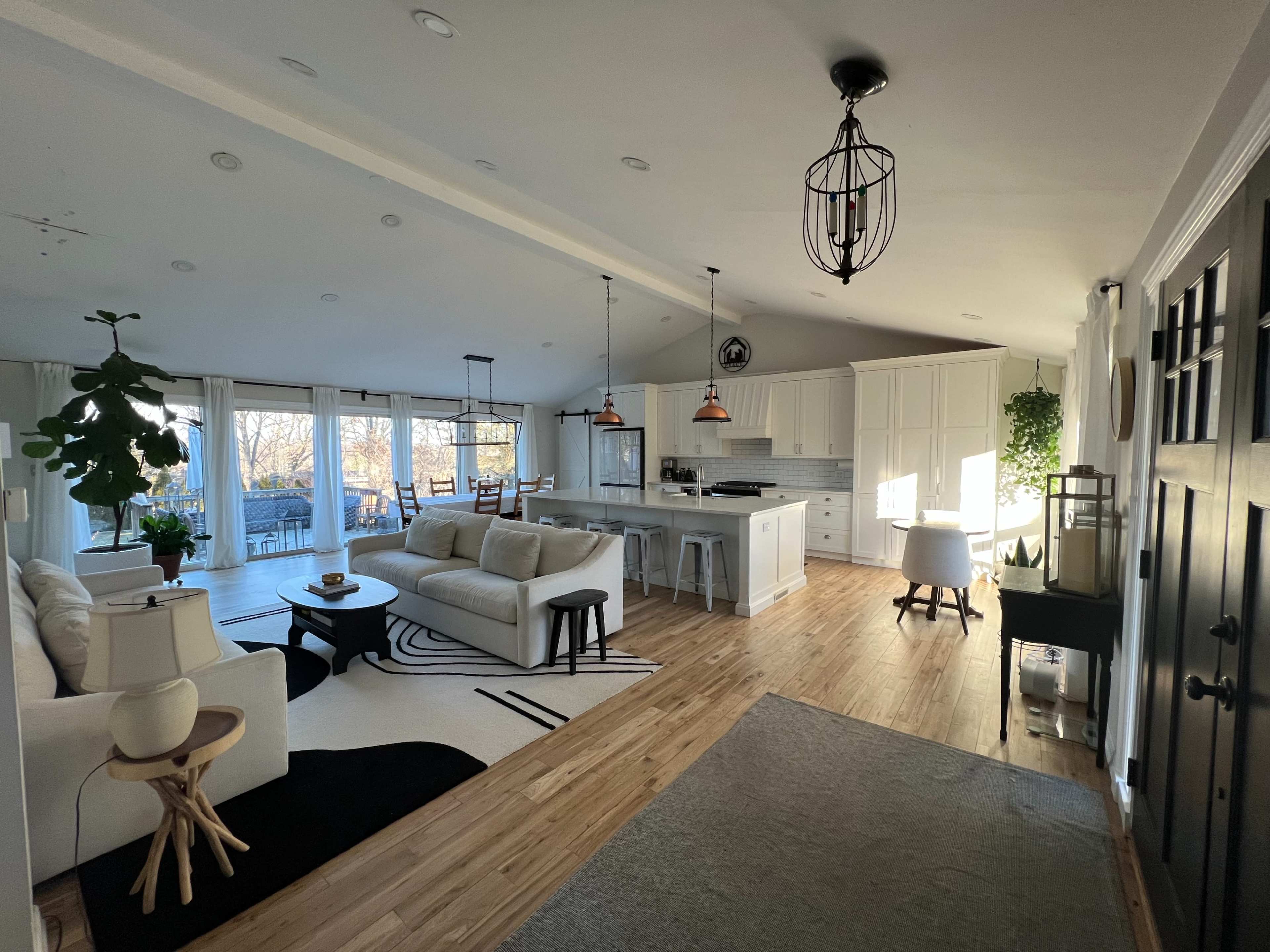 A spacious, well-lit living area with a modern kitchen, dining space, and large windows overlooking an outdoor view.