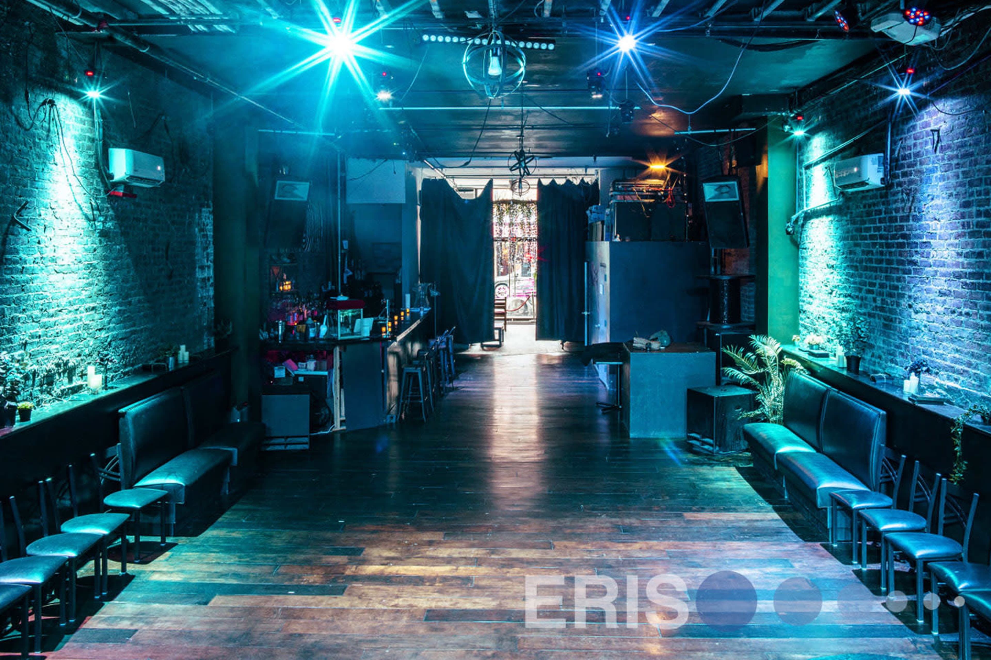 An indoor venue with wooden floors, blue and green lighting, and a bar area along one side.