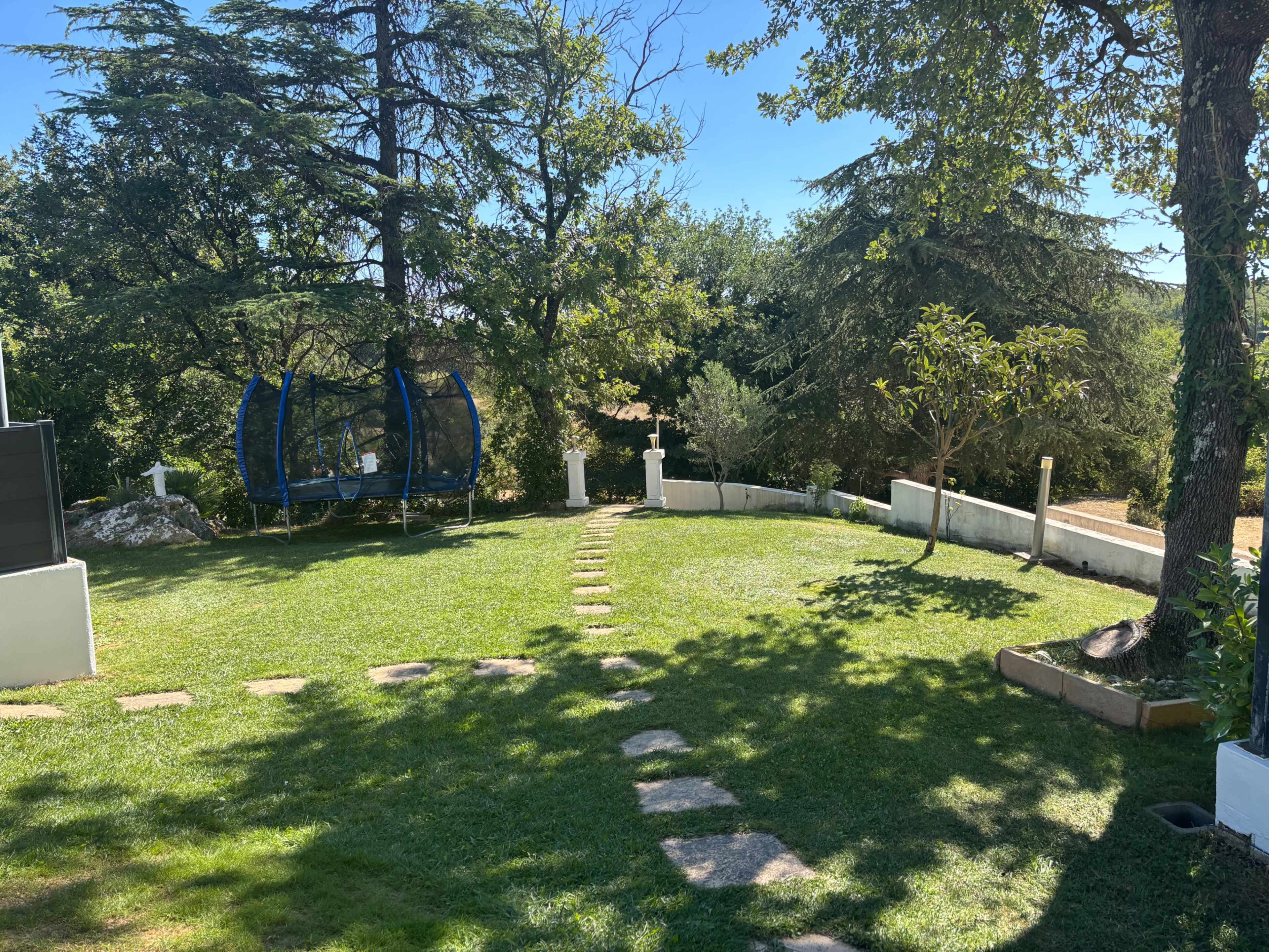 The image shows a green lawn with a pathway of stones leading through the garden, featuring a swing set under a large tree.