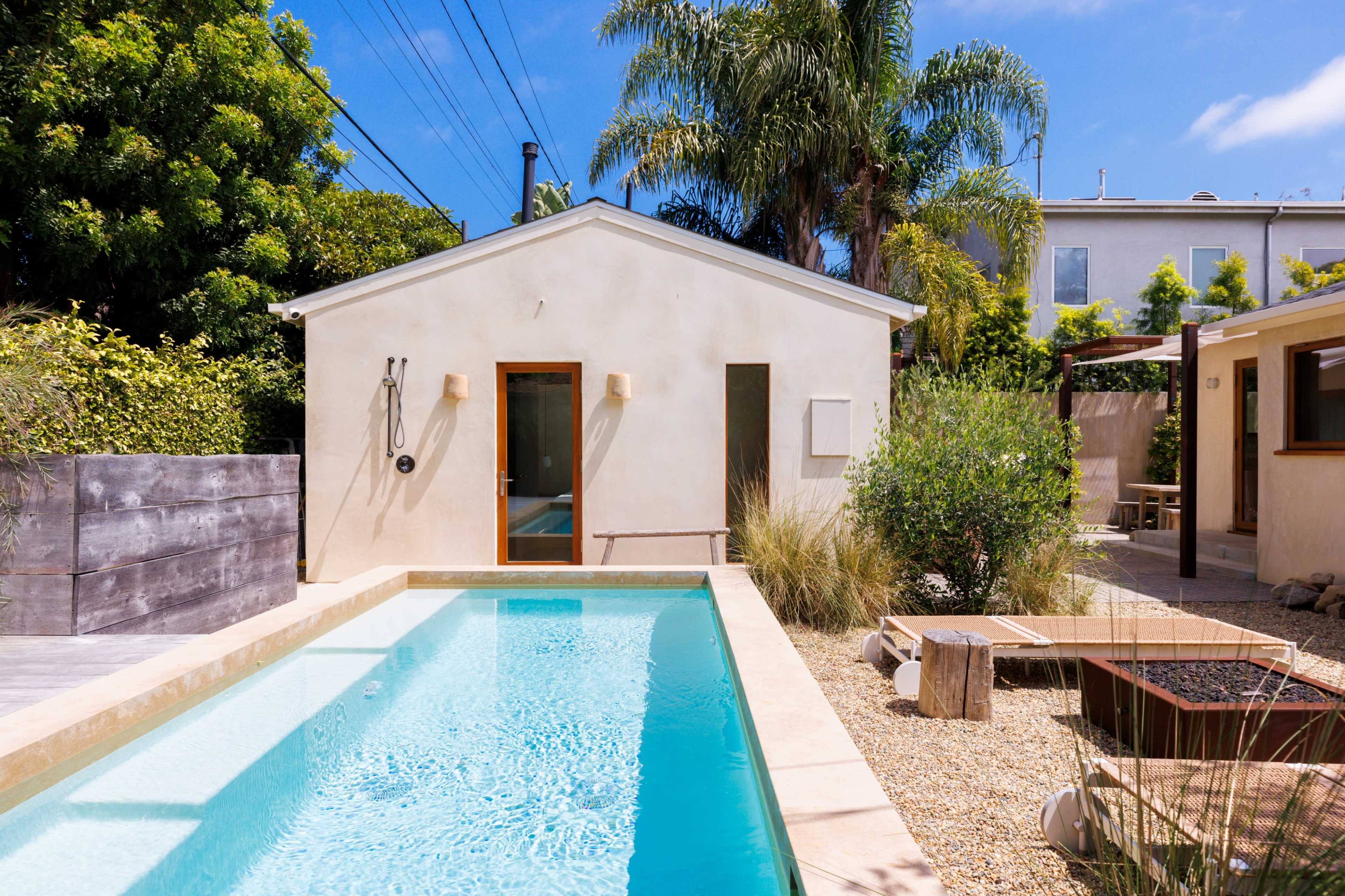 A modern backyard featuring a swimming pool alongside a small house, surrounded by greenery and outdoor seating areas.