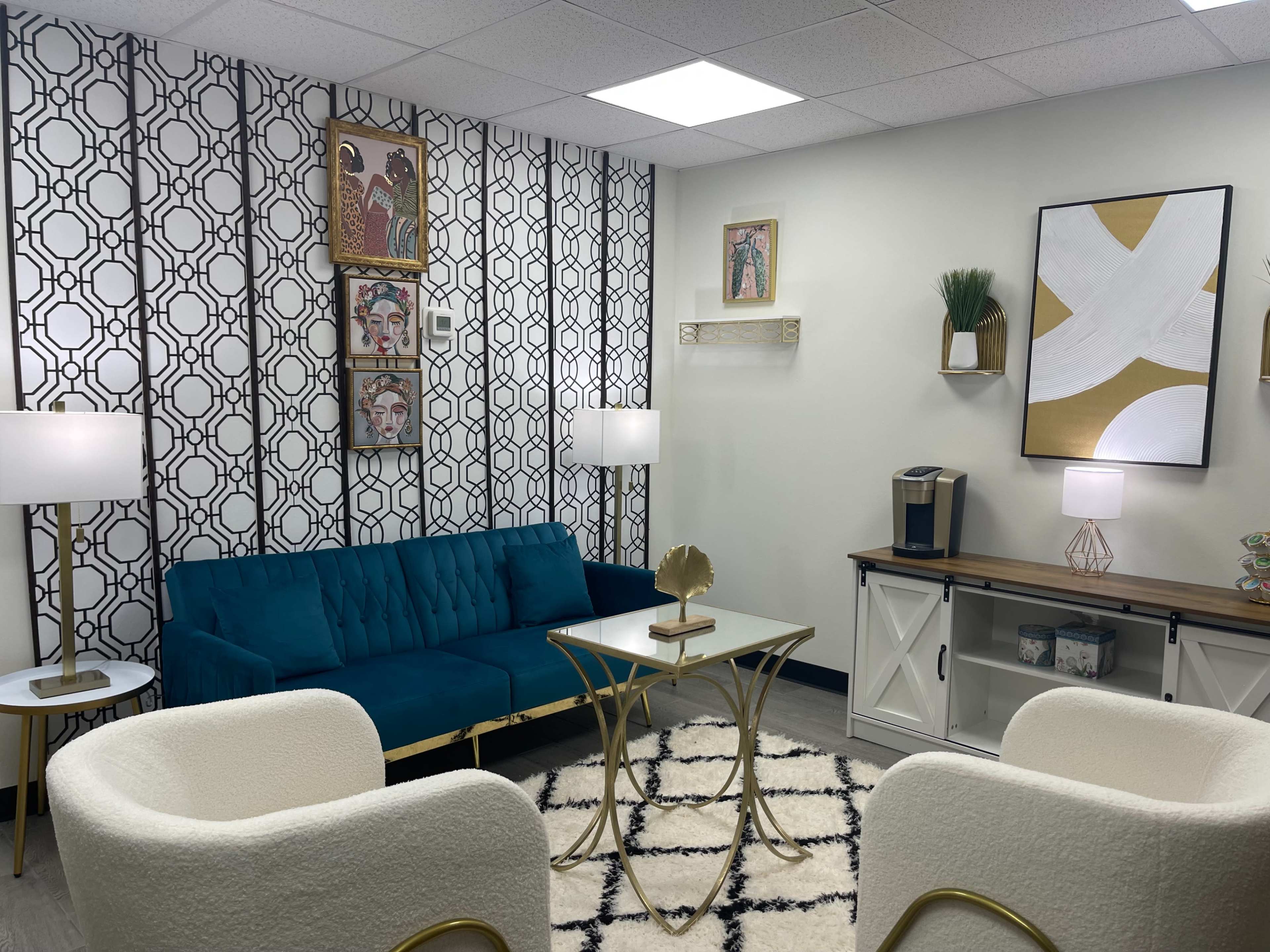 The image shows a modern lounge area featuring a teal sofa, two white armchairs, a coffee table, and decorative artwork on the walls.