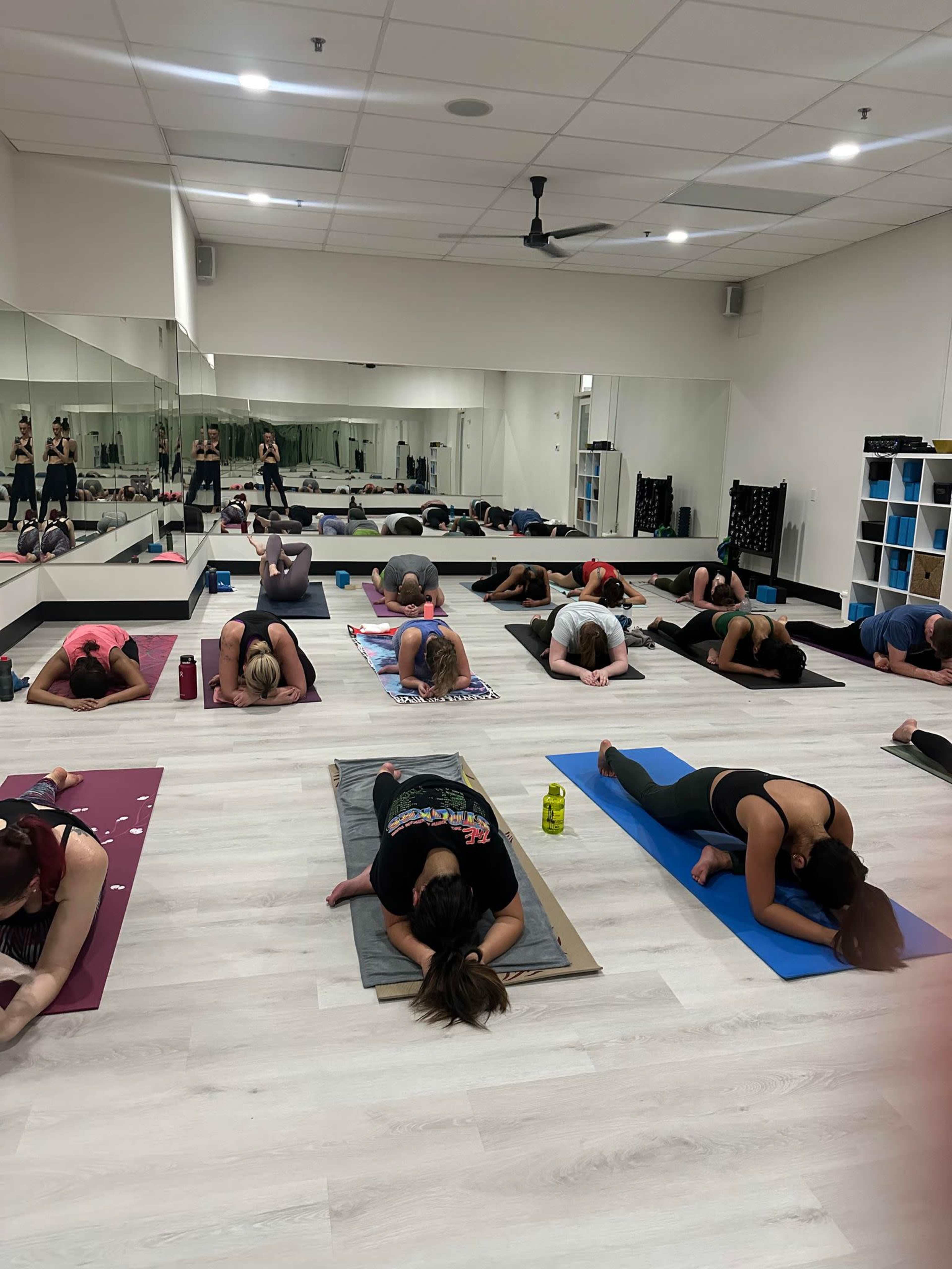 A group of individuals is practicing yoga in a mirrored studio, positioned on mats in various poses.
