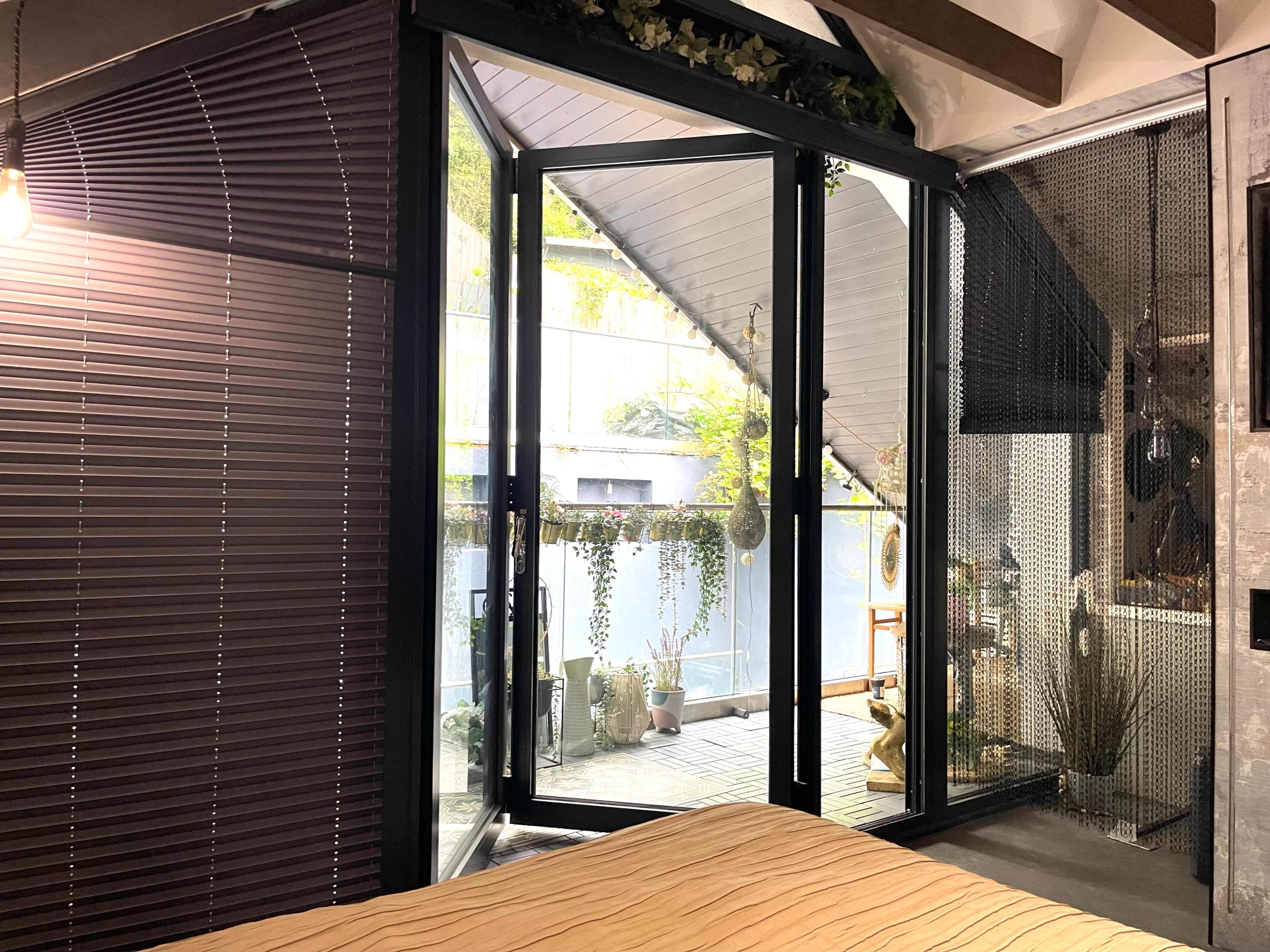 A modern bedroom with large glass doors leading to a deck adorned with plants and greenery.