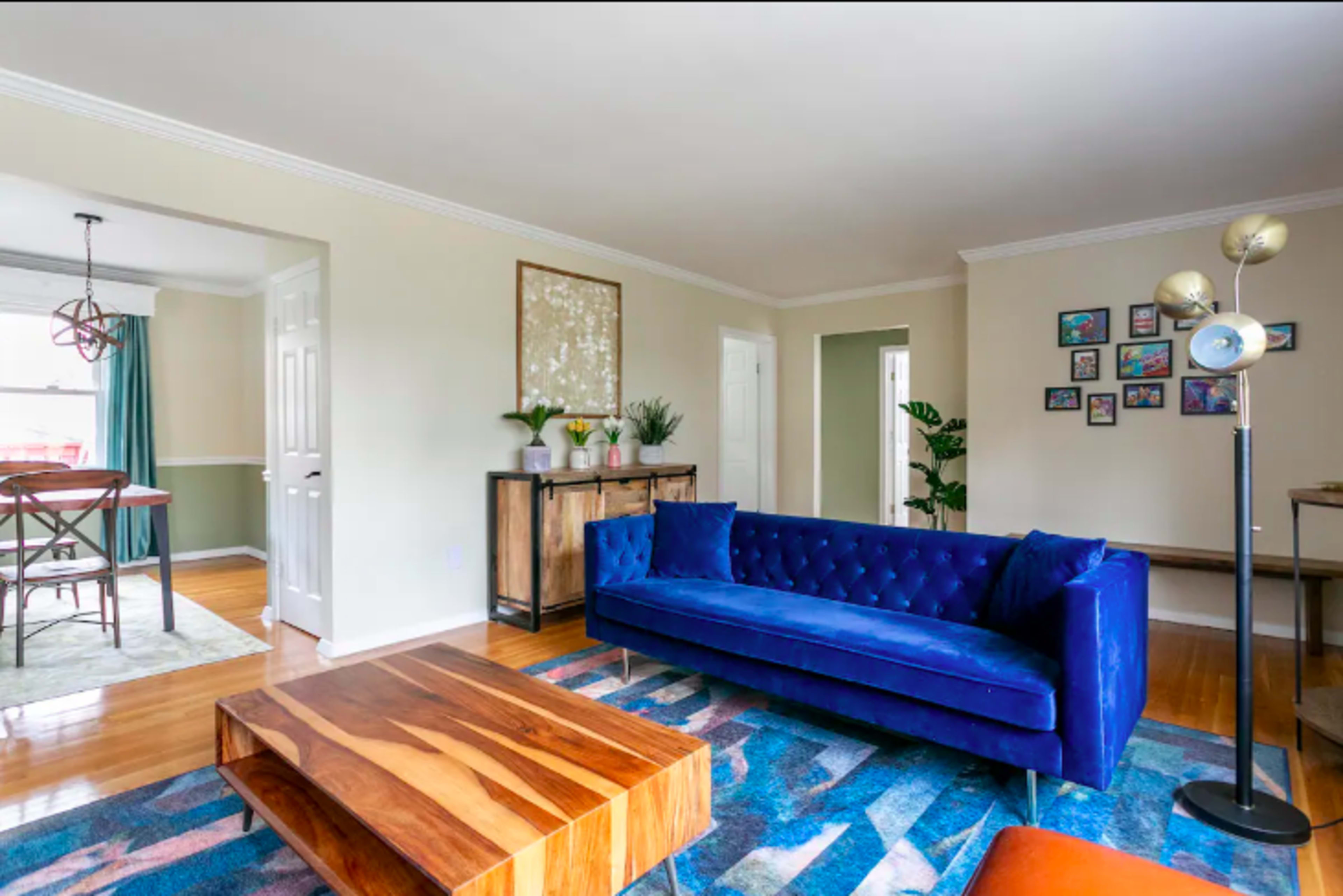 A living room with a blue velvet sofa, a wooden coffee table, and framed artwork on the walls.