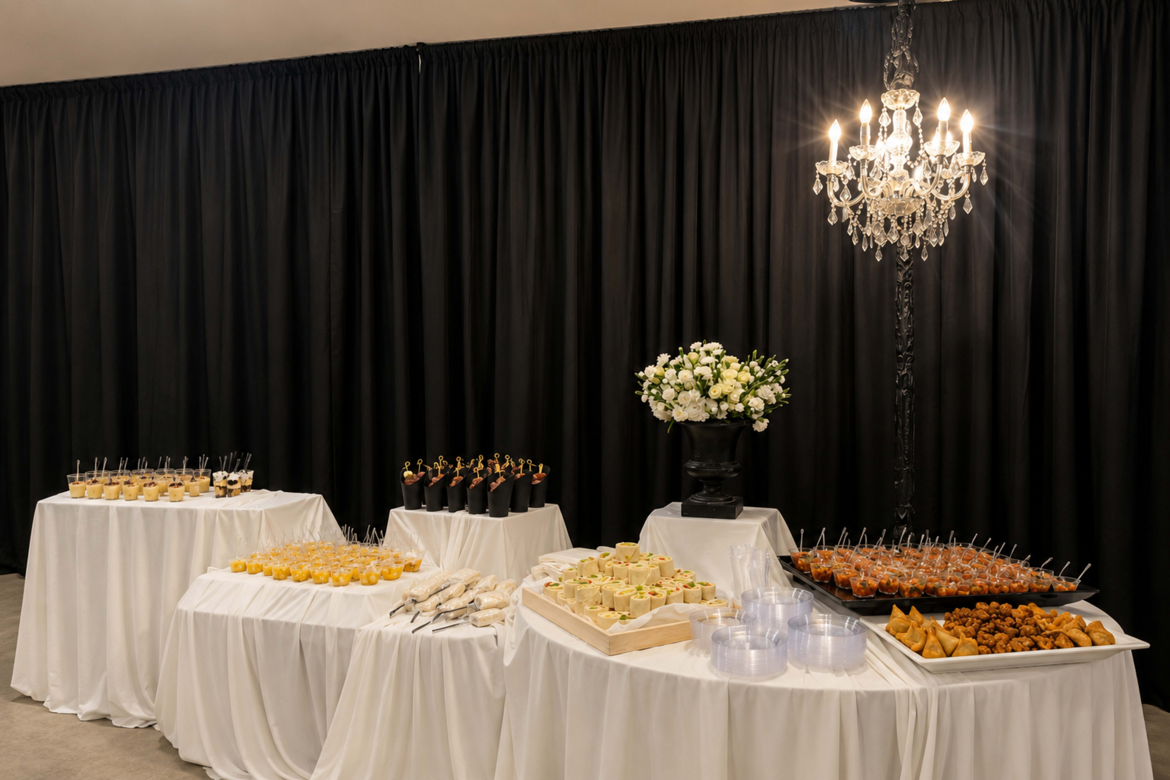 A buffet table is set with various elegantly arranged appetizers and desserts, adorned with a floral centerpiece and a chandelier overhead.