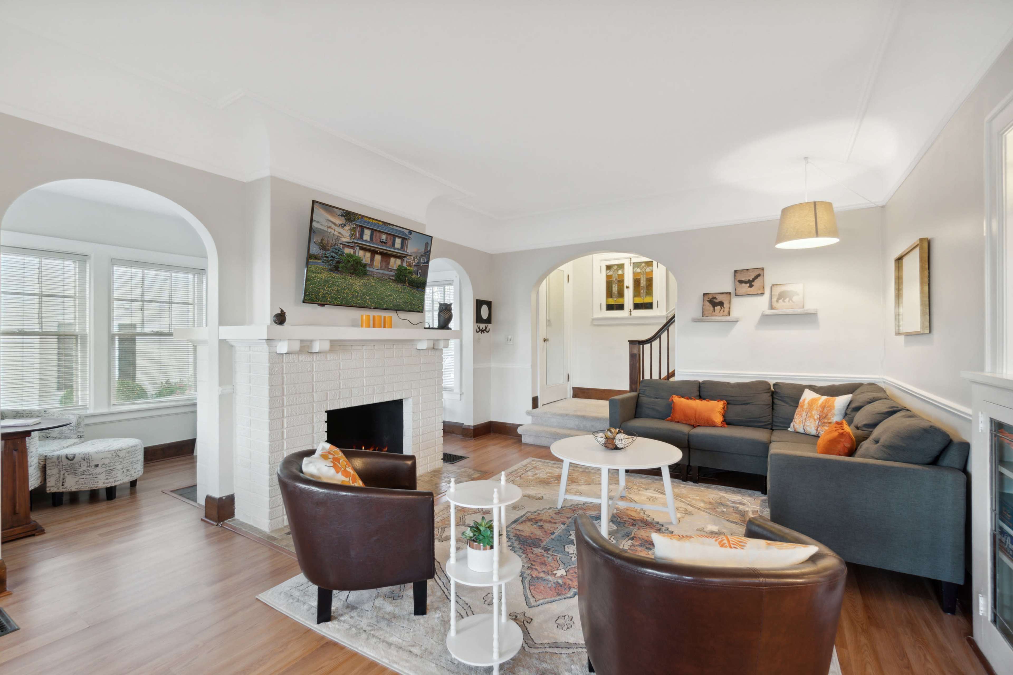 The image shows a living room featuring a fireplace with a television mounted above it, two armchairs, a coffee table, and an open layout connecting to adjacent spaces.