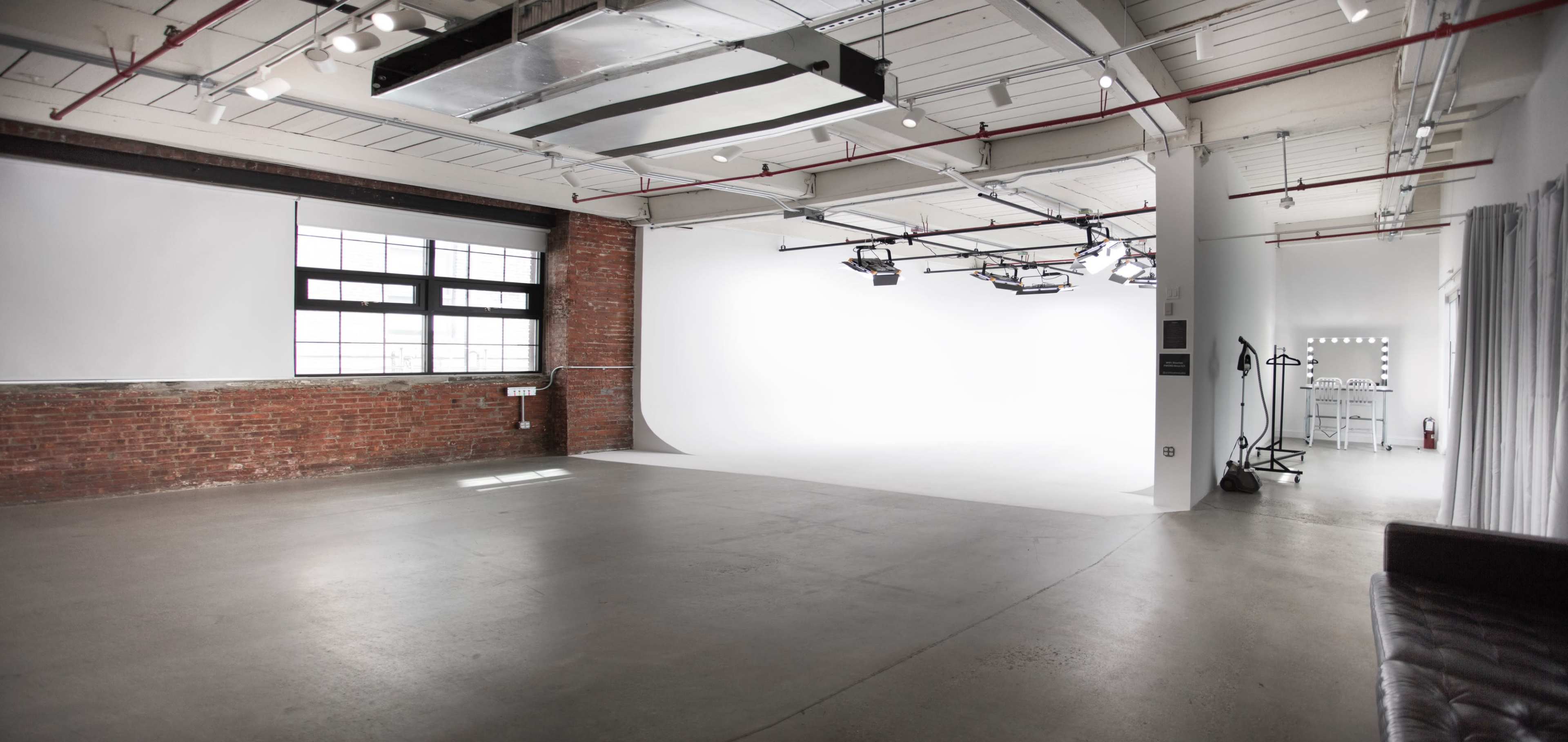 A spacious, minimalist studio with exposed brick walls, concrete flooring, and a large white backdrop.