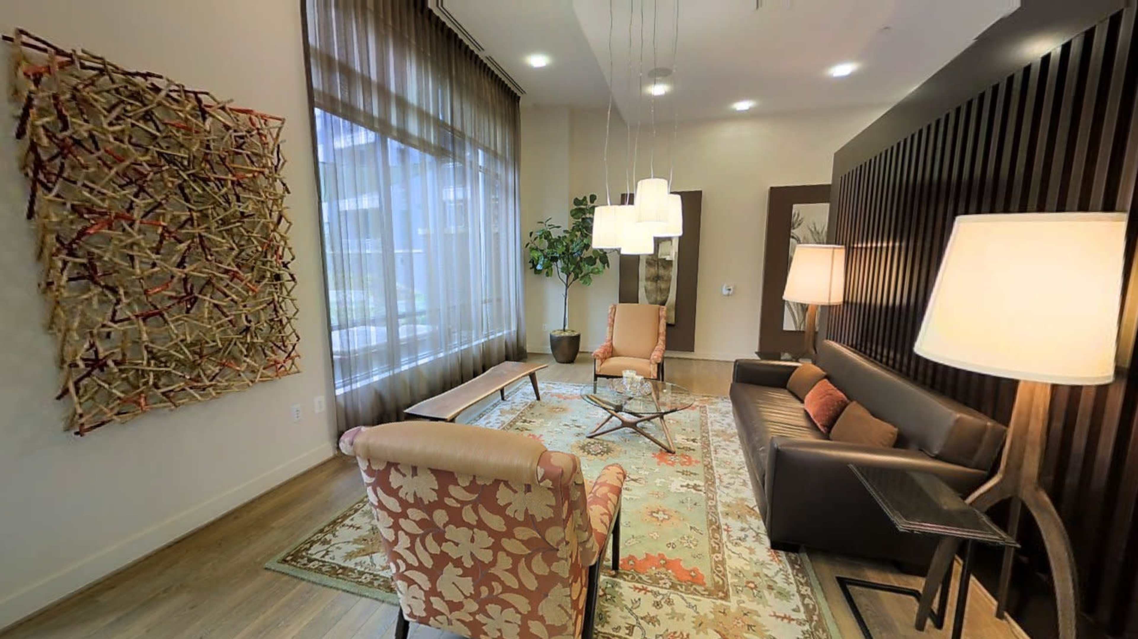 A modern sitting area featuring two upholstered chairs, a sofa, and artistic wall elements, illuminated by pendant lights.