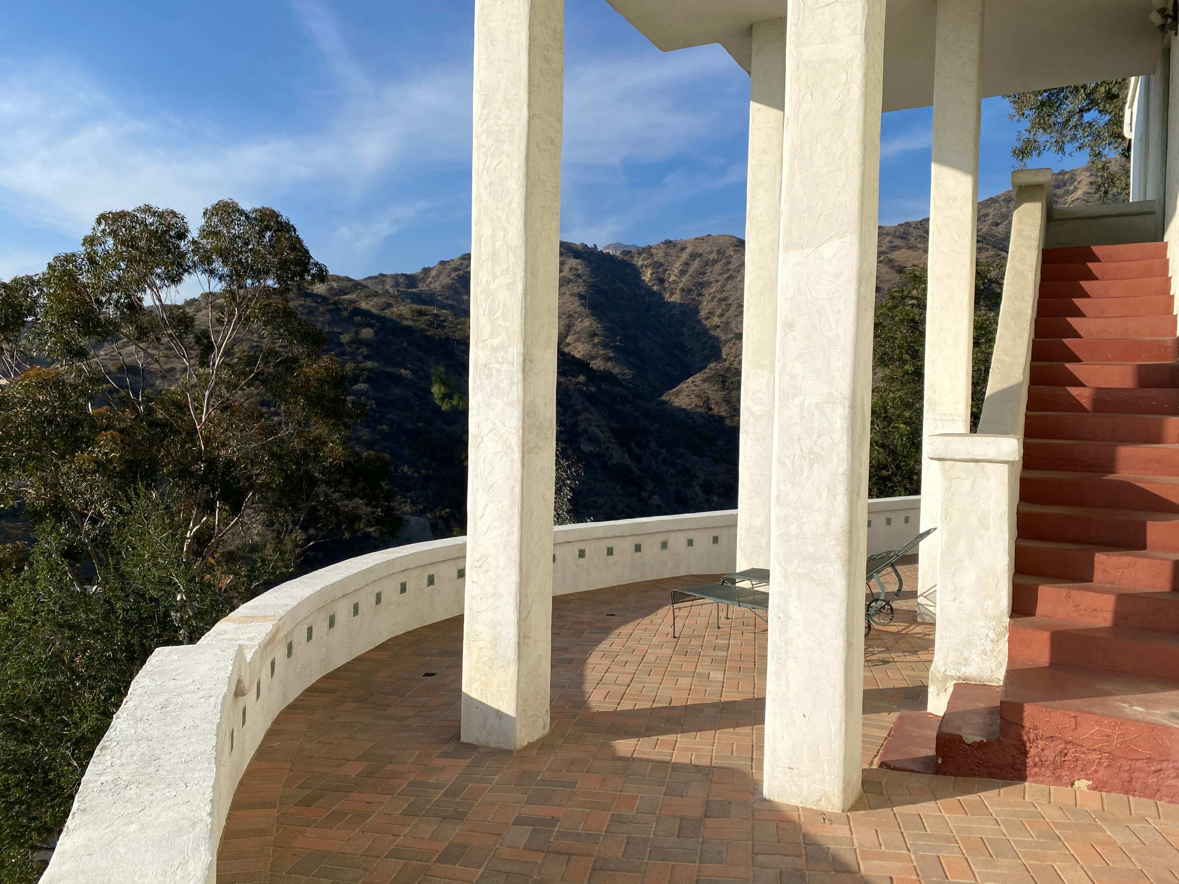 A terrace with white columns and a staircase, overlooking a mountainous landscape under a clear blue sky.
