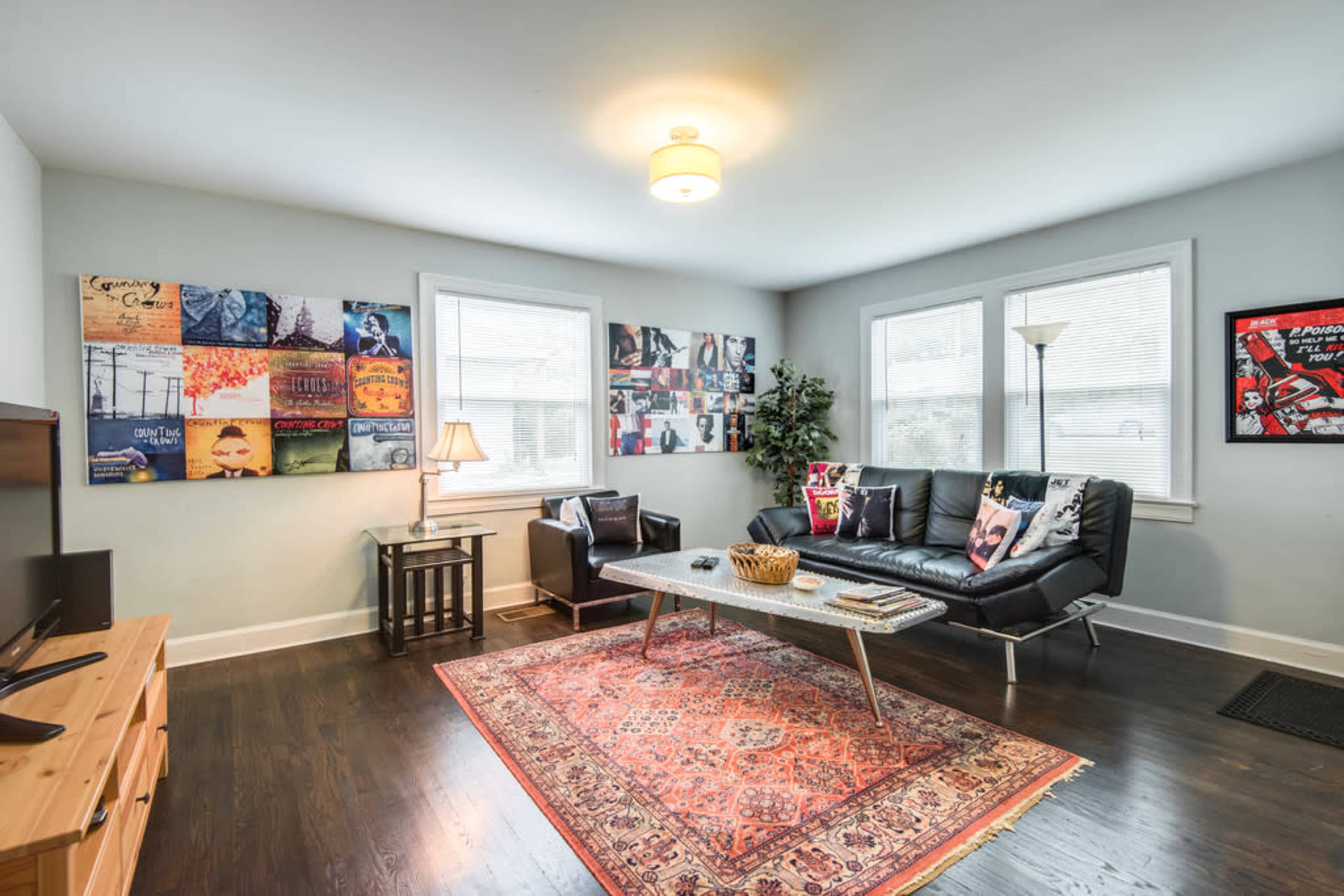 The living room features a black leather sofa, a coffee table, a rug, and walls adorned with framed artwork.
