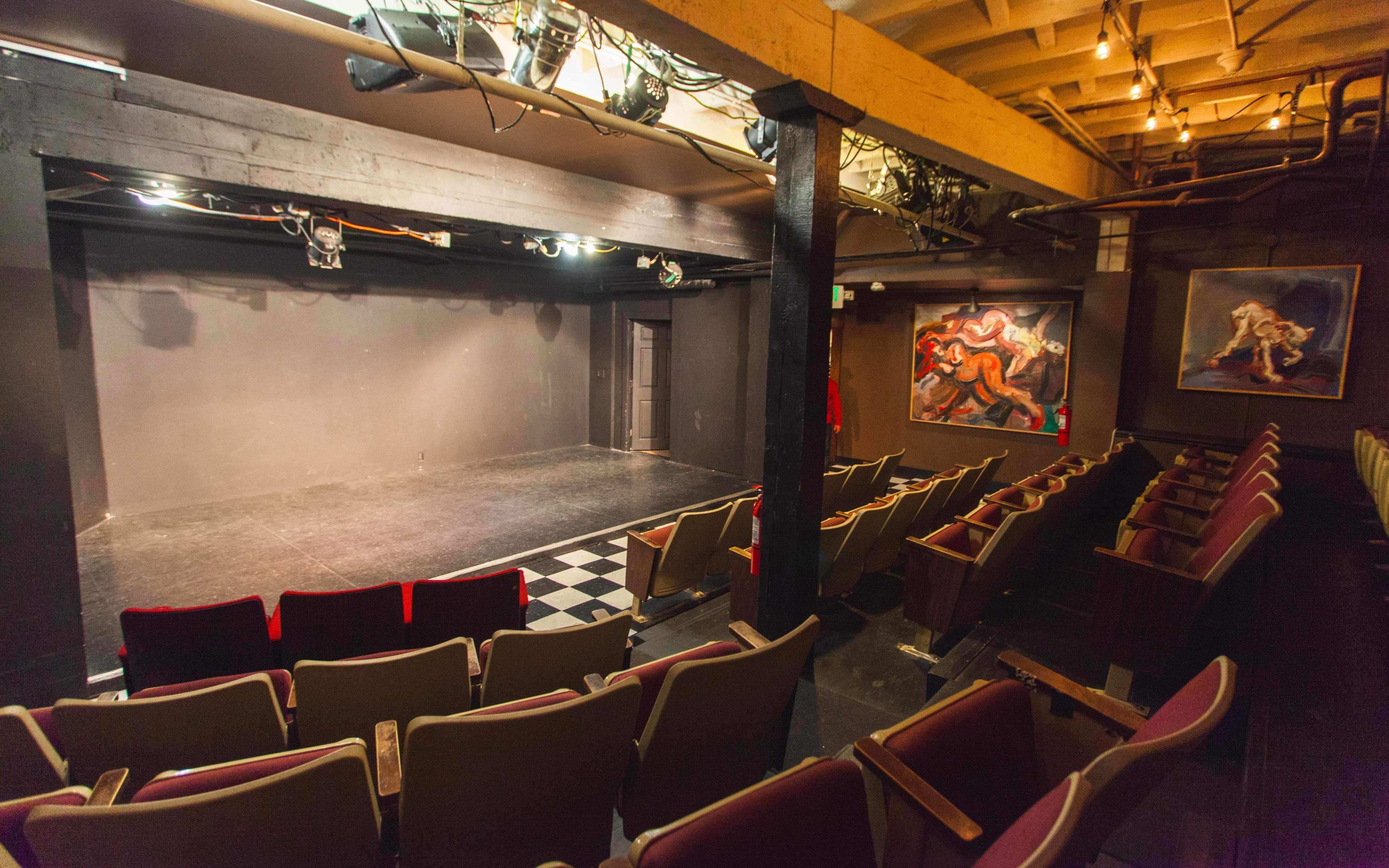 A small theater with a dimly lit stage and an empty audience area featuring rows of seats.