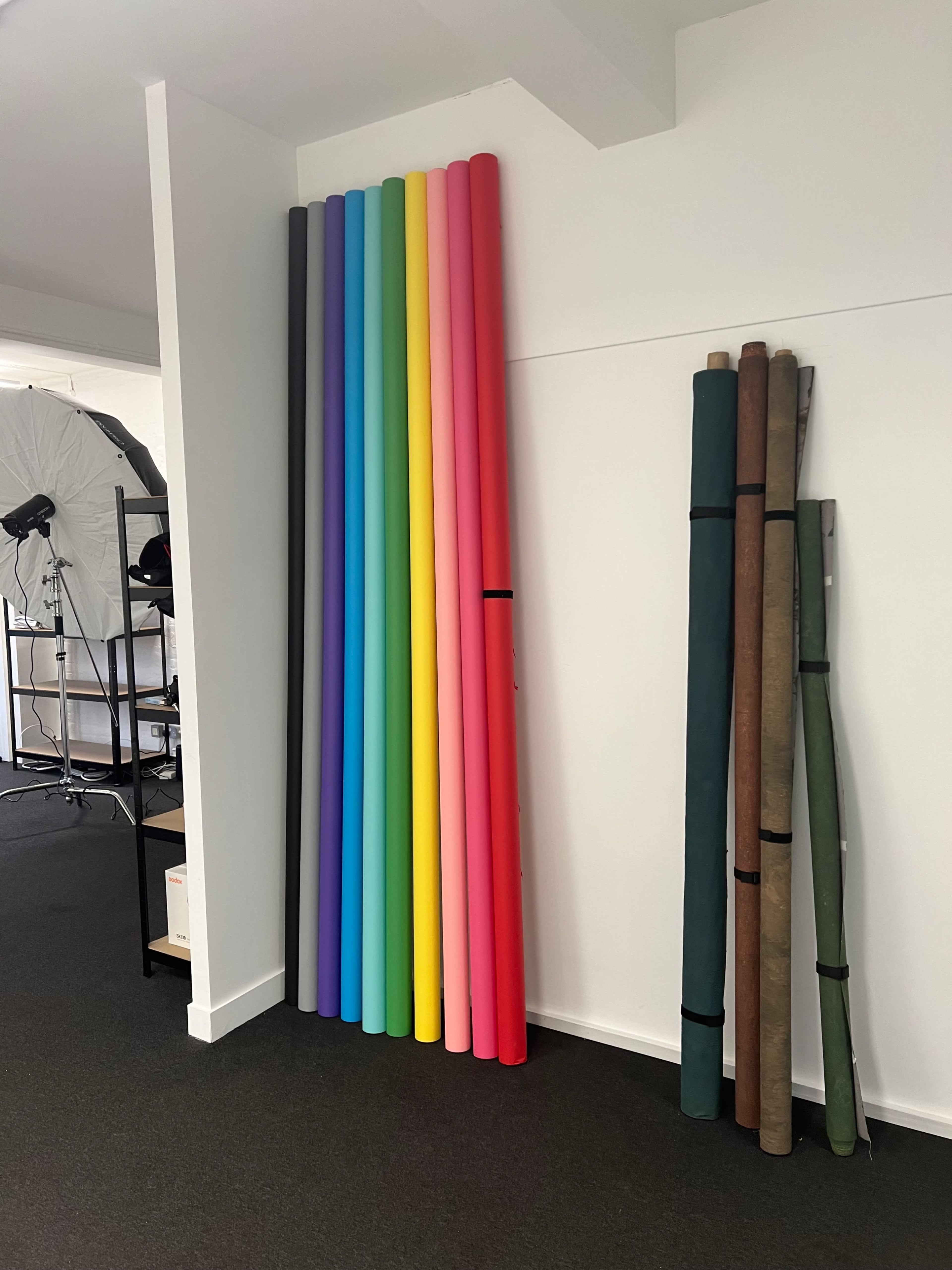 A collection of colorful backdrop rolls stacked against a white wall, with additional rolls in muted colors leaning nearby.