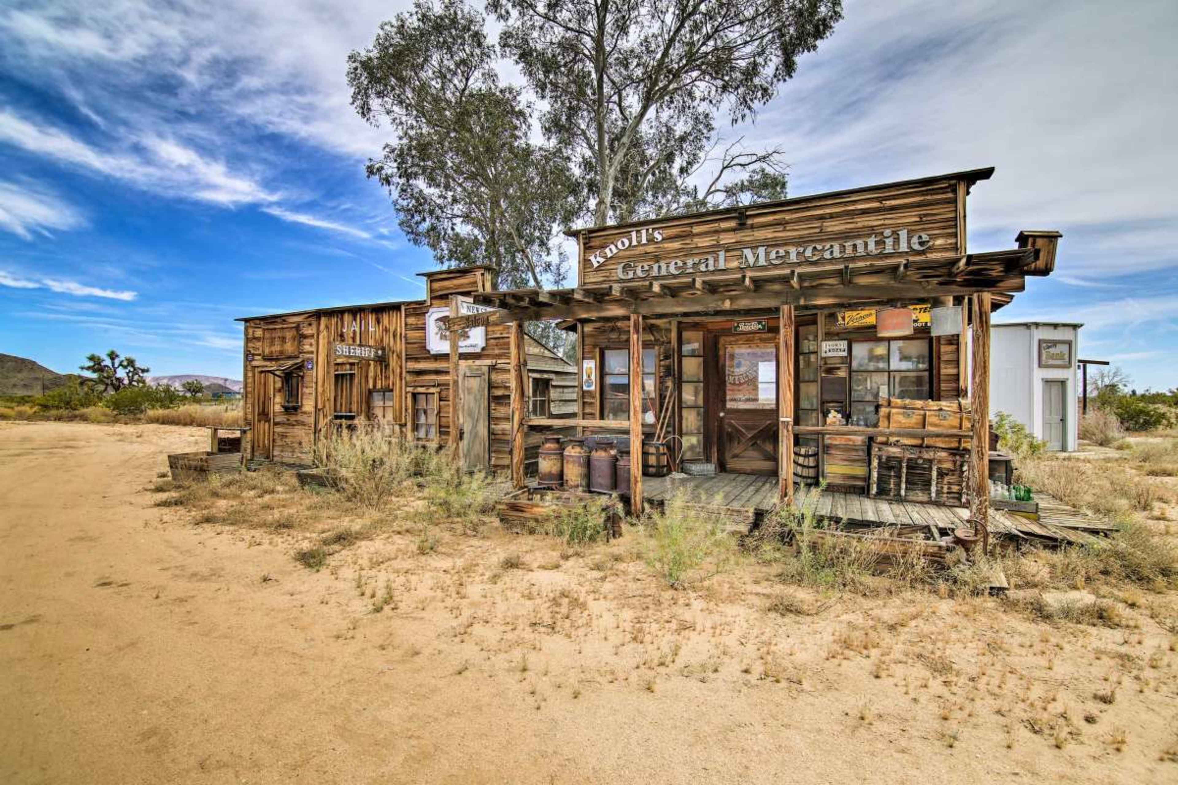 A weathered wooden general mercantile storefront set in a dry, sandy landscape with sparse vegetation.