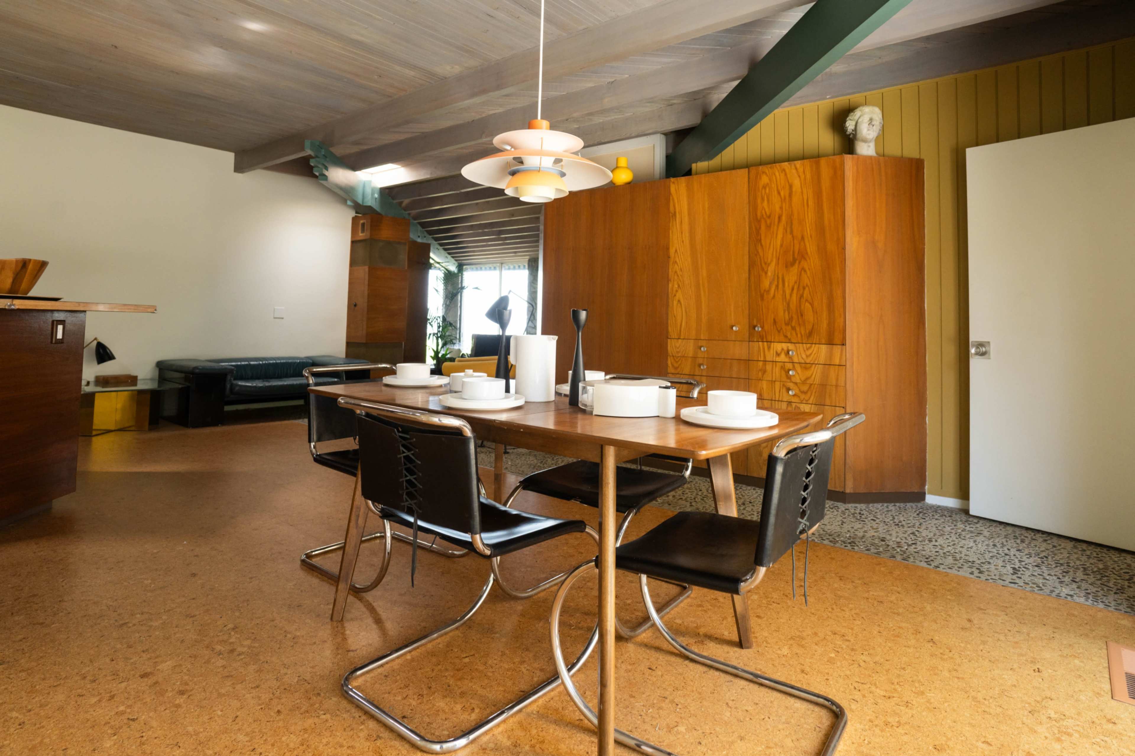 A dining table with four chairs is set for a meal in a modern kitchen with wooden cabinets and a decorative pendant light.