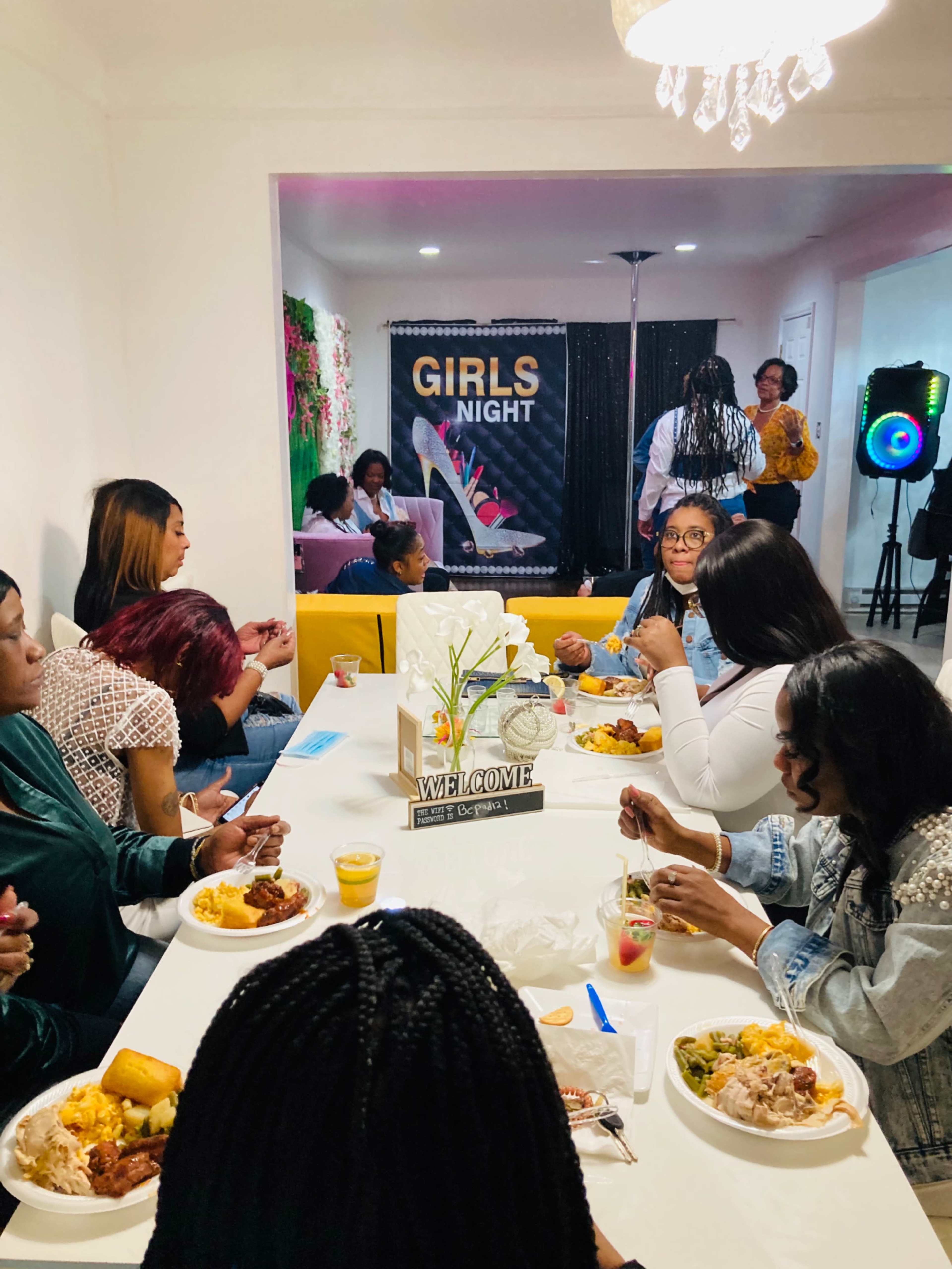 A group of women gathered around a table, enjoying a meal during a "Girls Night" event in a brightly lit room.