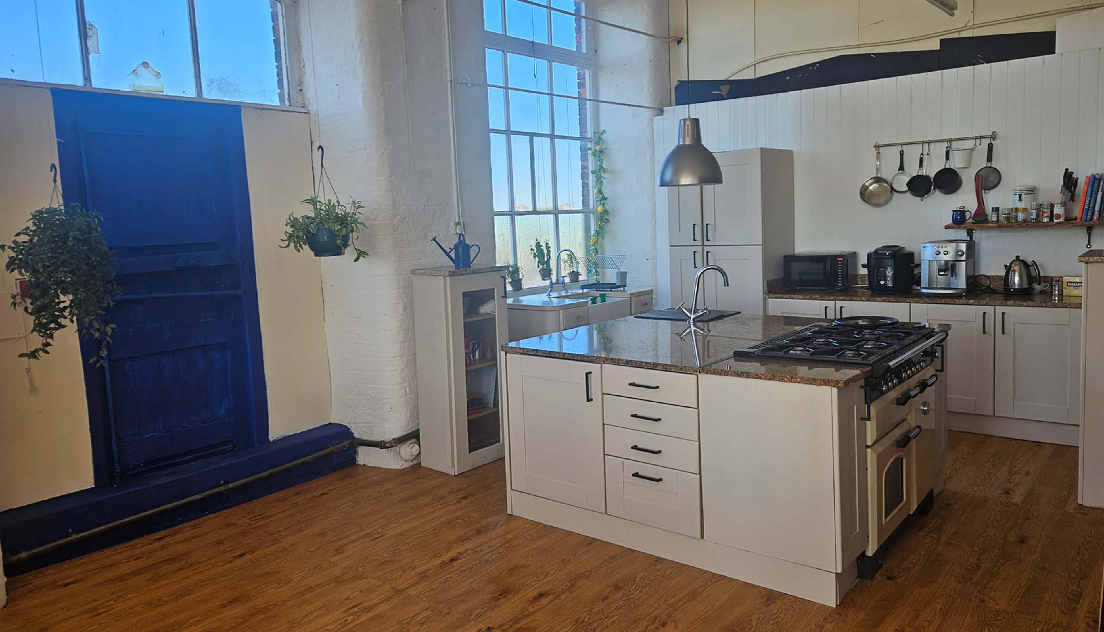 The image shows a bright kitchen featuring a central island with a stove, white cabinetry, and large windows that let in natural light.