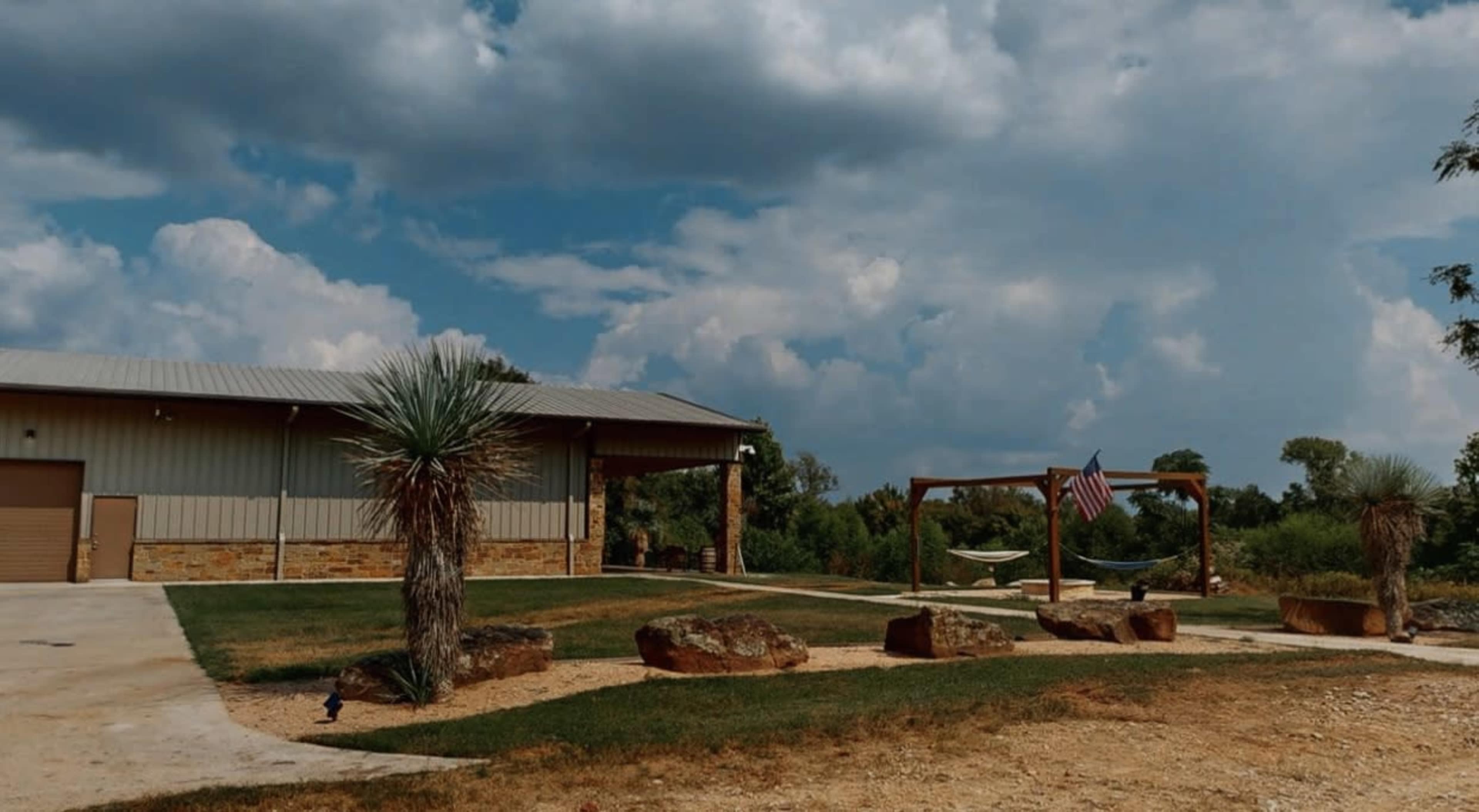 A modern building with a metal roof is situated next to a grassy area featuring large rocks and a flag hanging from a wooden swing set.