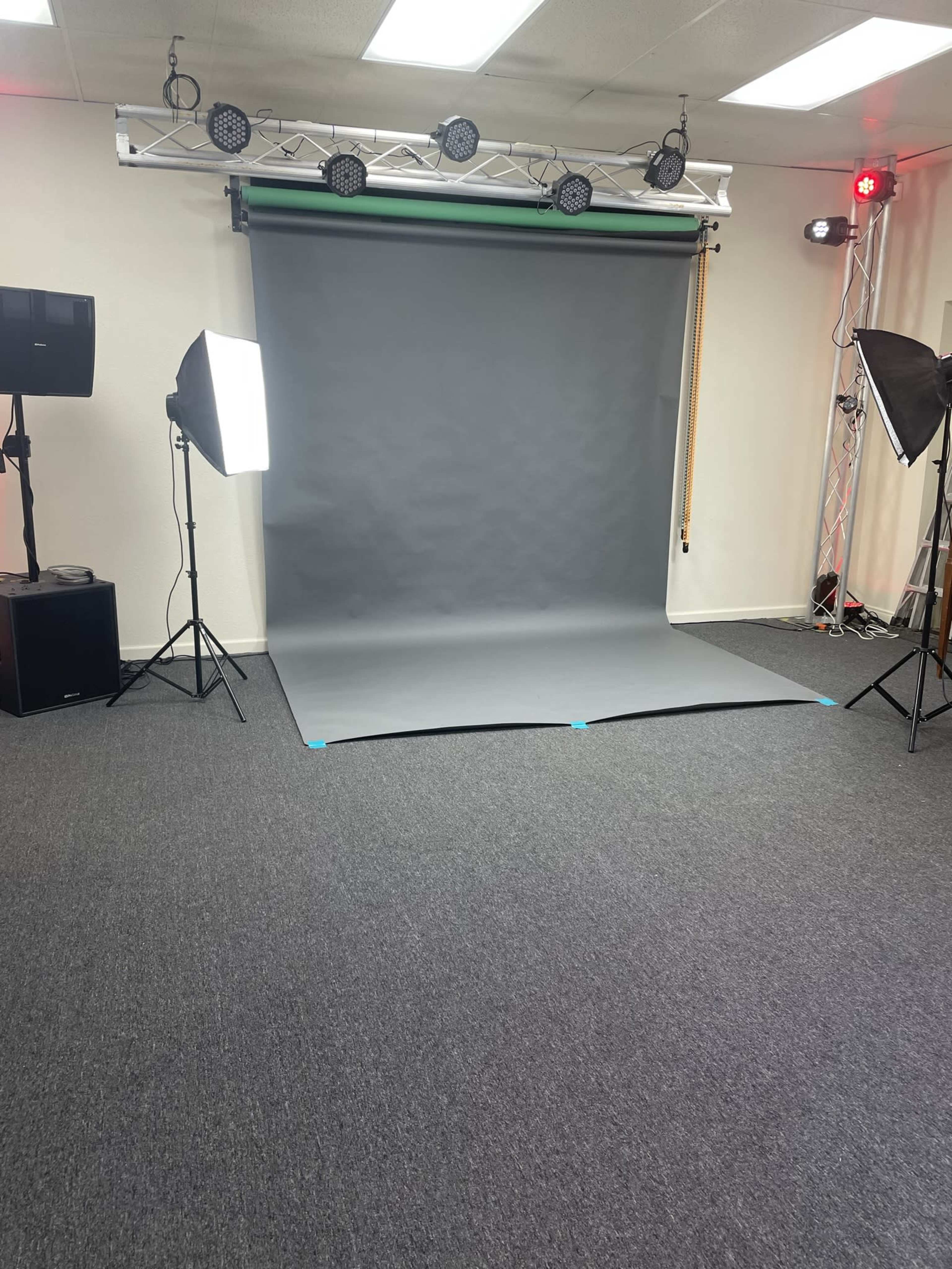 A photography studio with a gray backdrop set up, lighting equipment on both sides, and a clean carpeted floor.