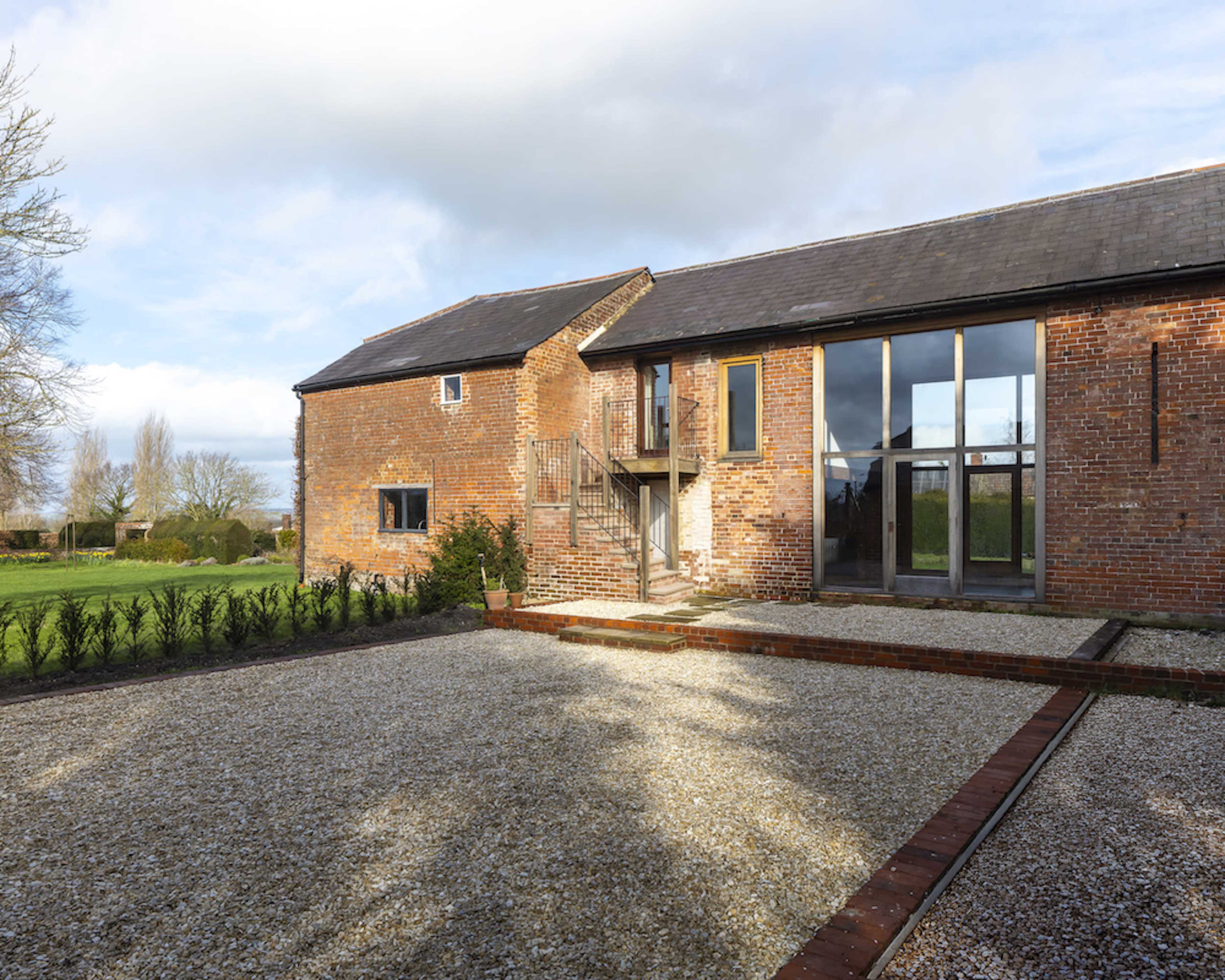 A renovated brick barn features large windows and a gravel courtyard surrounded by manicured landscaping.