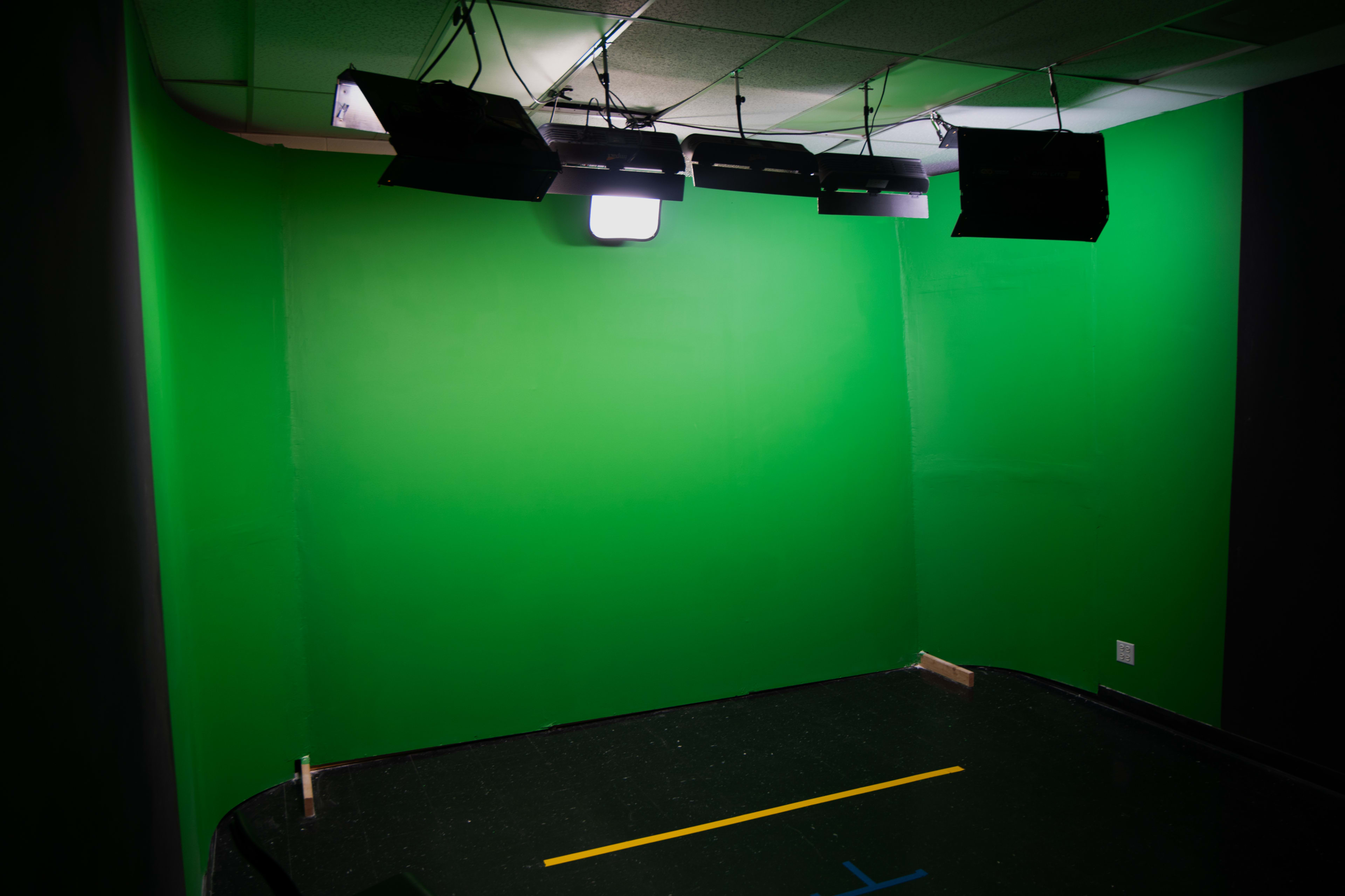 A room with a green screen backdrop illuminated by overhead lights.