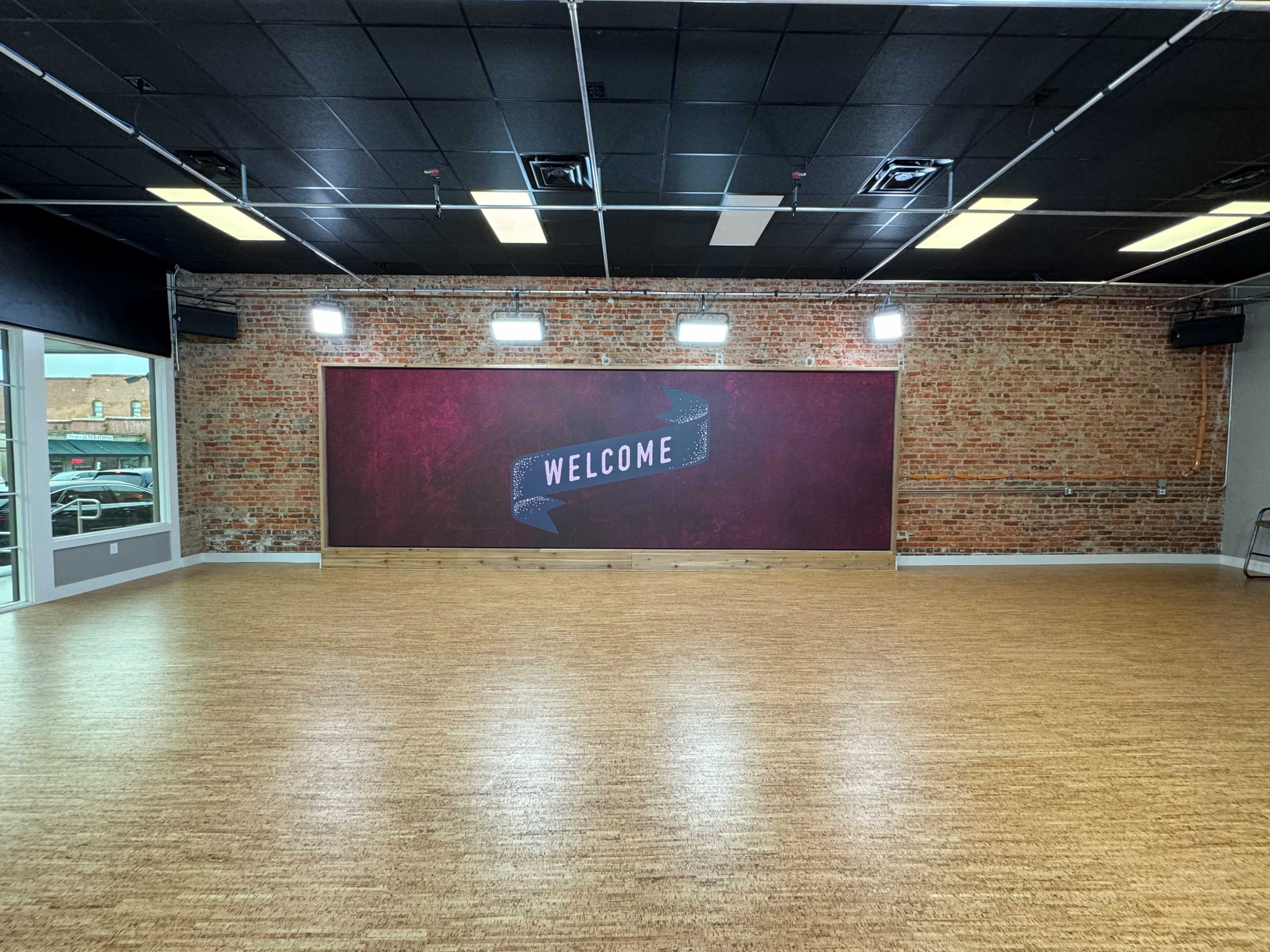 A spacious room with a wooden floor and a red brick wall featuring a "WELCOME" sign.
