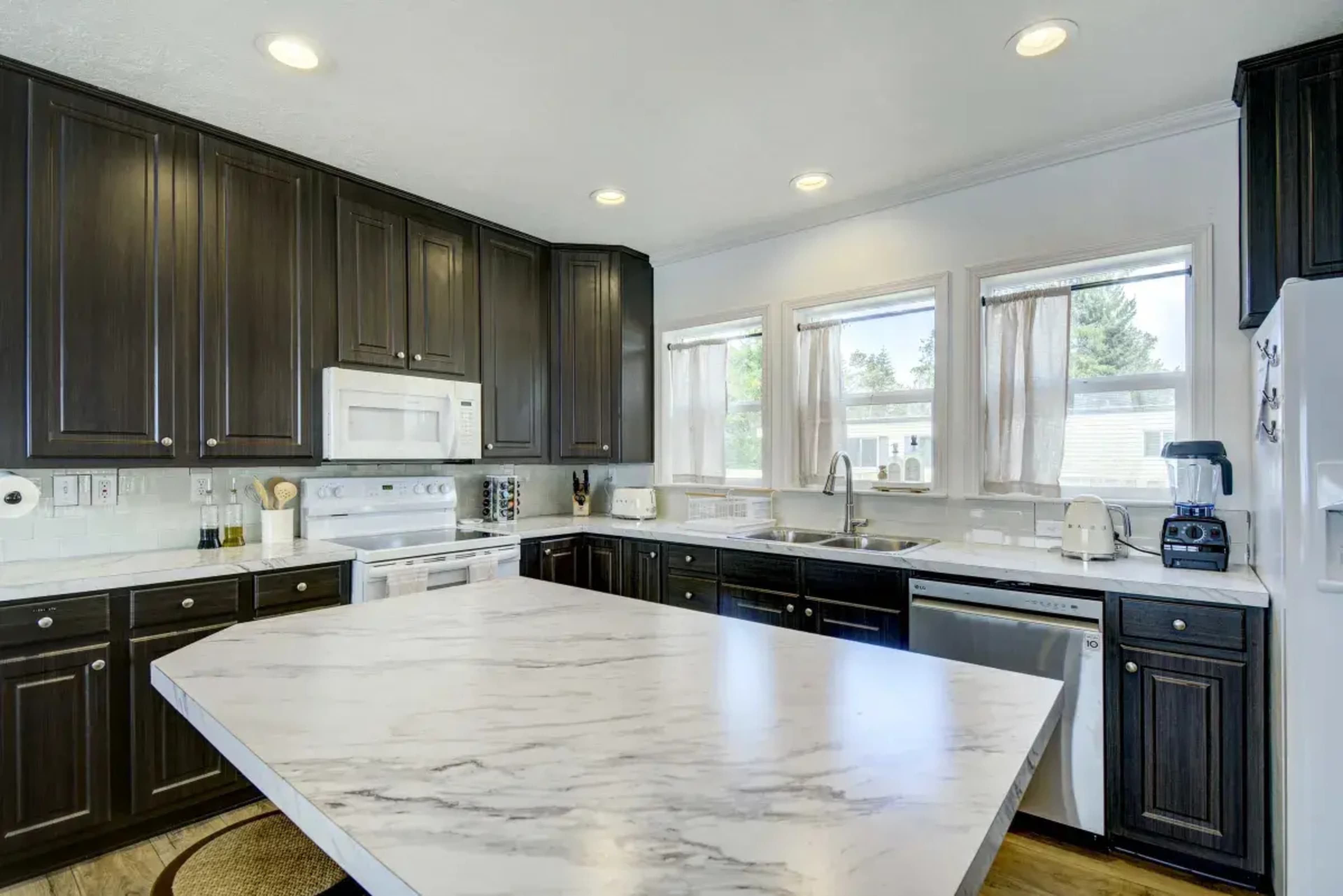 A modern kitchen features dark cabinetry, marble countertops, and stainless steel appliances, with ample natural light from the windows.