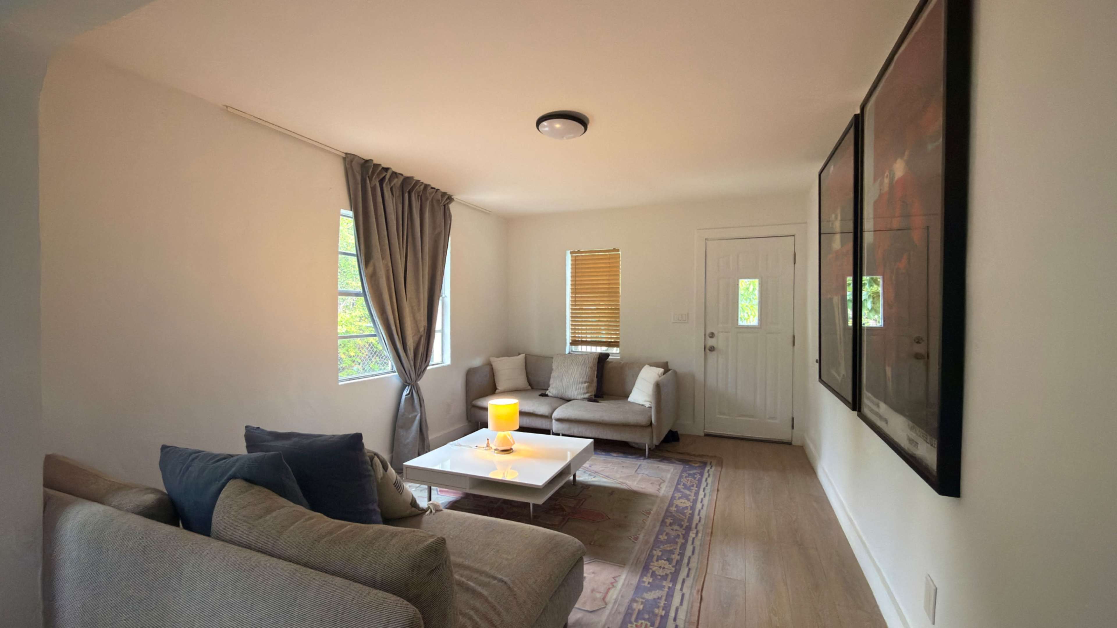 The image shows a well-lit living room with two sofas, a small coffee table, and a door leading outside.