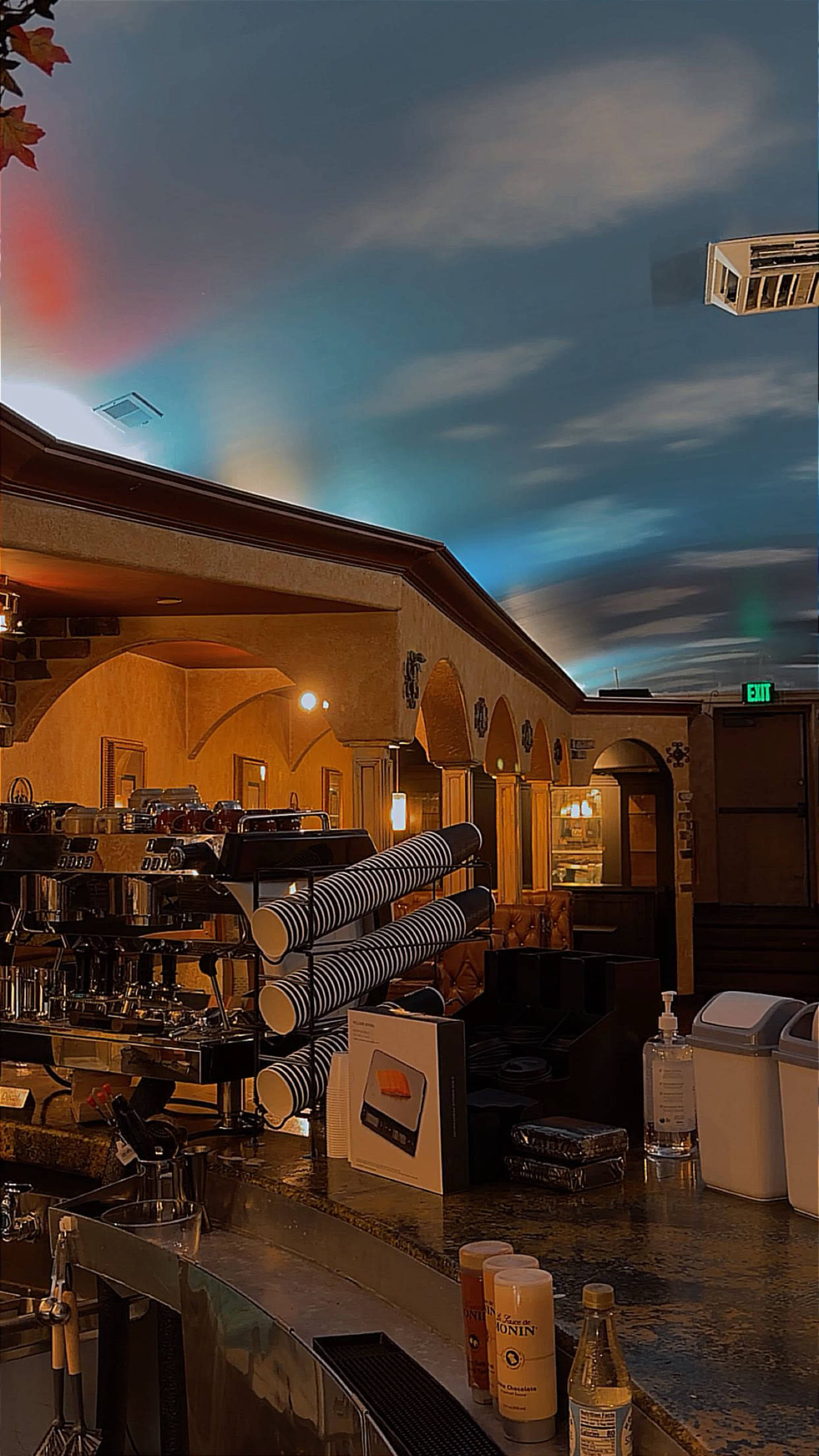The image shows a coffee shop interior with a coffee machine, stacked cups, and a ceiling painted to resemble a sky.